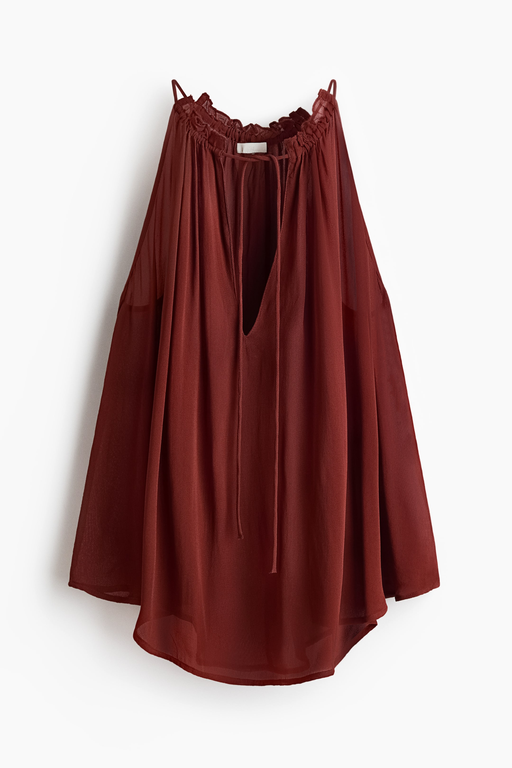 View larger image: A flowing rust-coloured top is showcased from the front, featuring a gathered neckline with thin spaghetti straps and a deep V-neck with delicate ties. Its sheer fabric drapes loosely to a curved hem.