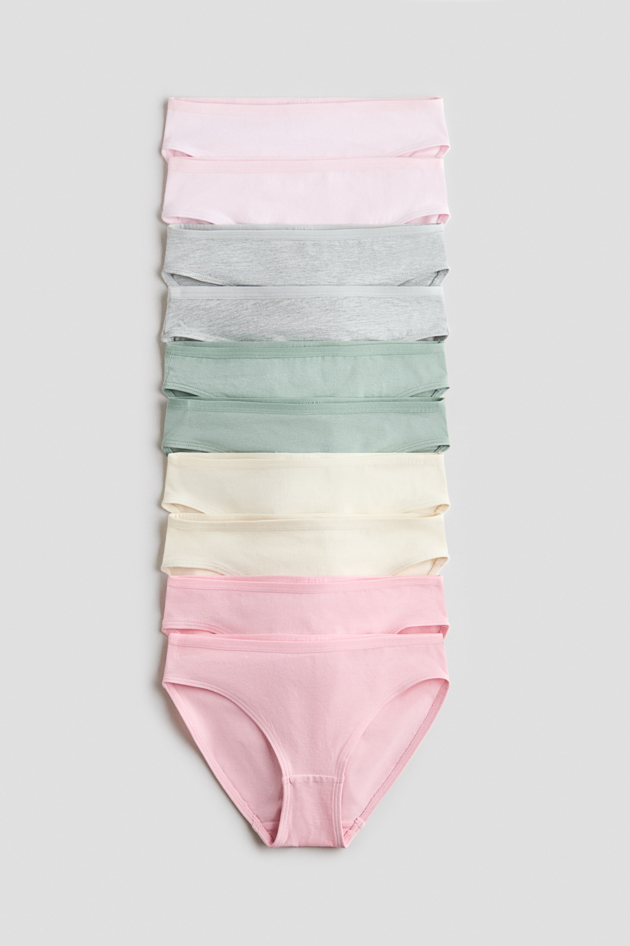 Ver imagen más grande: Bragas de suave algodón de jersey se exhiben en una pila vertical, presentando varios colores pastel, incluyendo rosa claro, gris claro, verde claro y crema claro. Las bragas inferiores muestran una vista frontal, destacando su cintura elástica y las aberturas de las piernas.