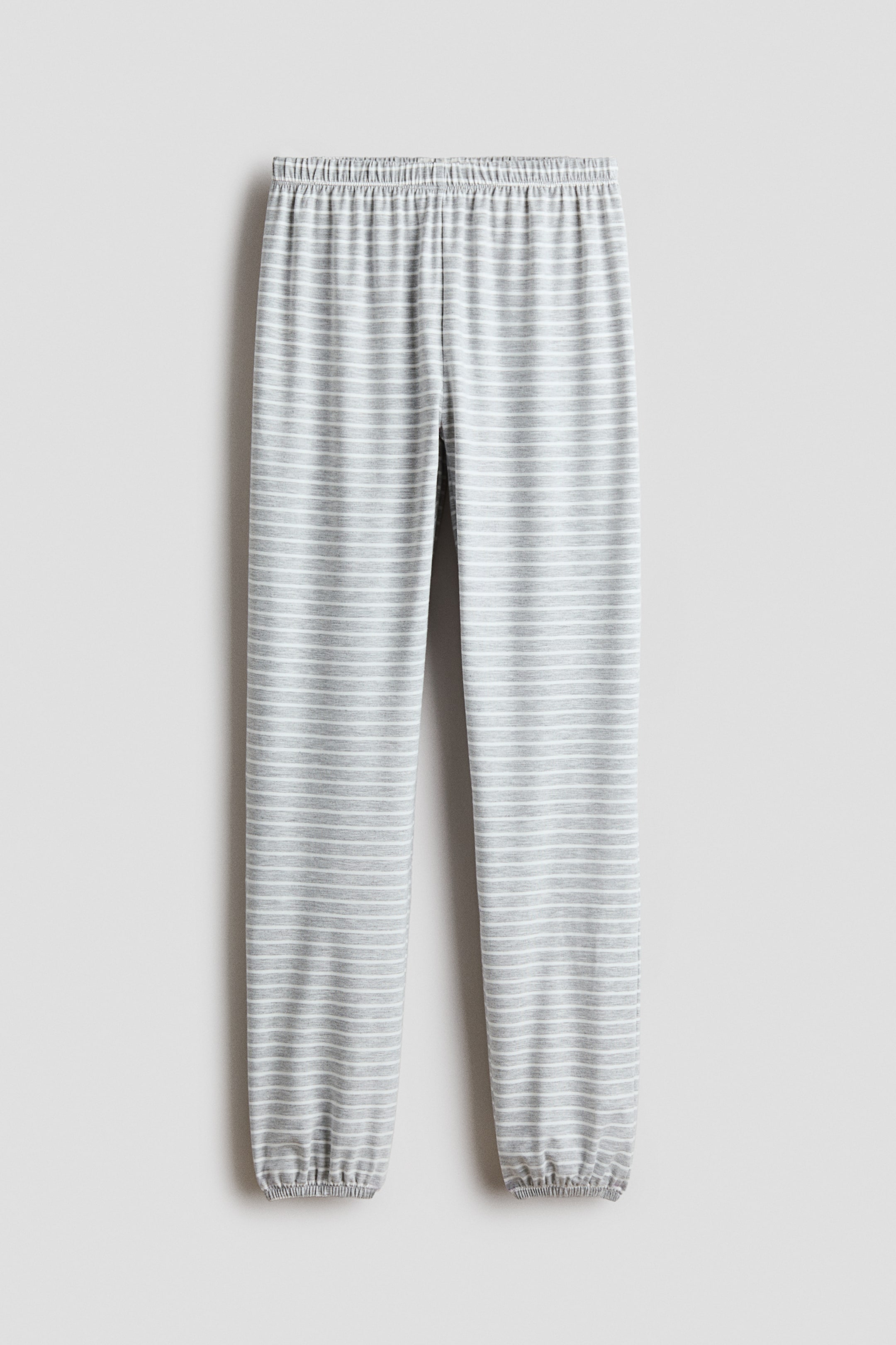 View larger image: A pair of grey and white horizontally striped joggers is shown from the front, featuring a gathered elasticated waistband and relaxed legs with elasticated ankle cuffs.