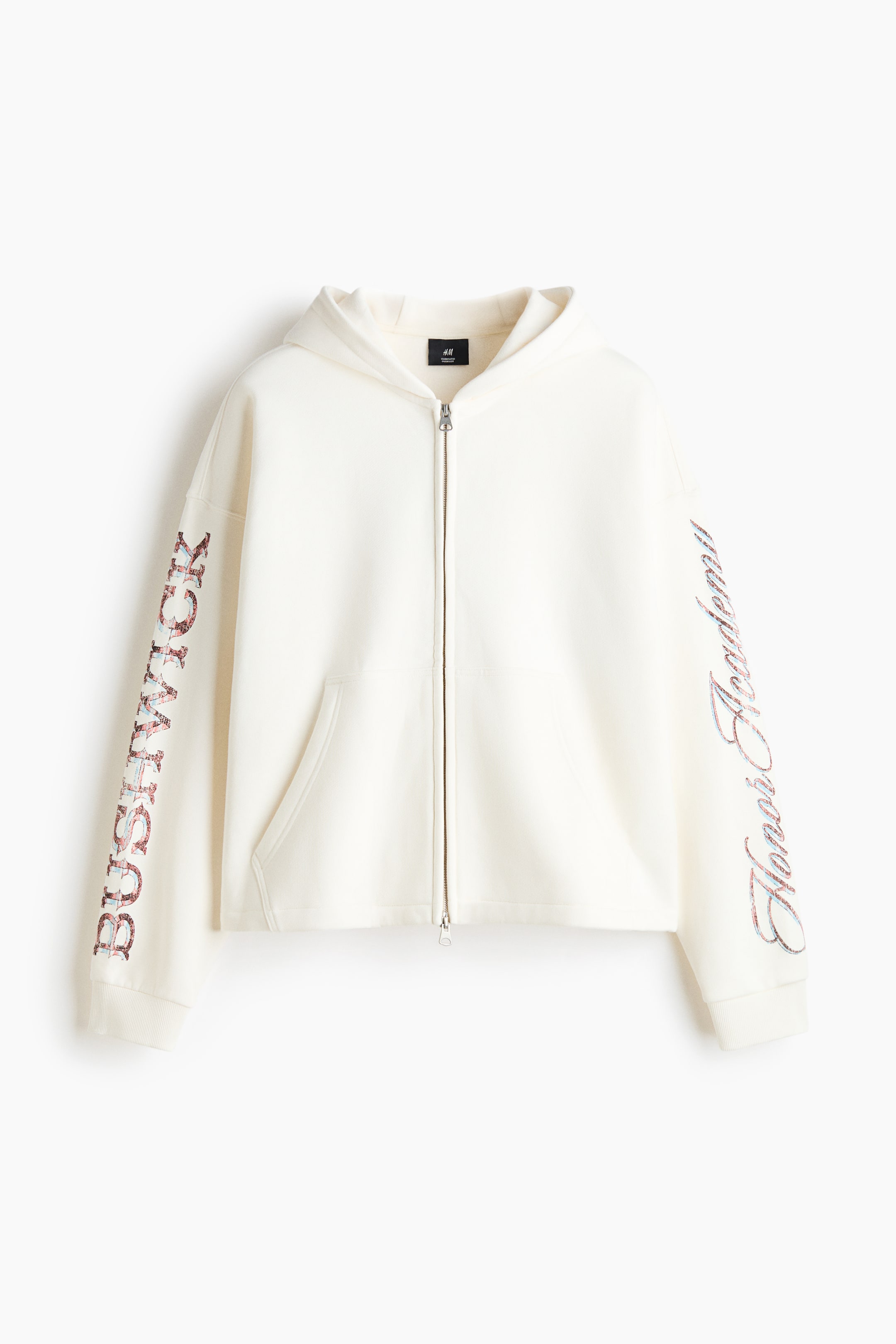 Visualizza l'immagine ingrandita: Una felpa con cappuccio zip-up color crema è mostrata frontalmente, mettendo in evidenza una zip argentata, una tasca a marsupio divisa e polsini a coste. La manica destra riporta la scritta "BUSHWICK" in caratteri block, mentre la manica sinistra presenta il testo corsivo "Honor Academy" in un design multicolore.