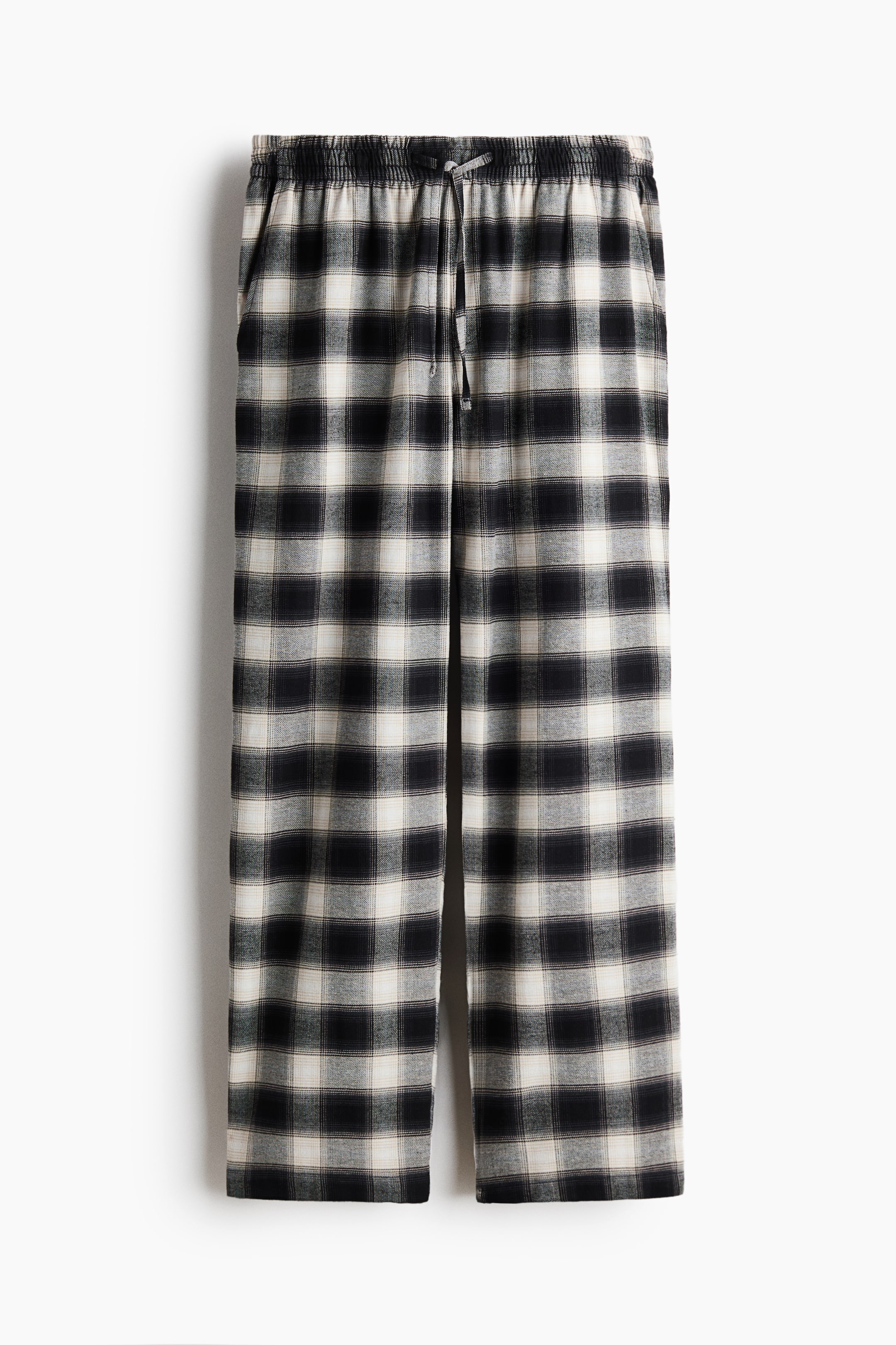 View larger image: The plaid flannel trousers feature an elasticated drawstring waist and diagonal side pockets, displaying a black and off-white pattern in a relaxed, front-facing view.