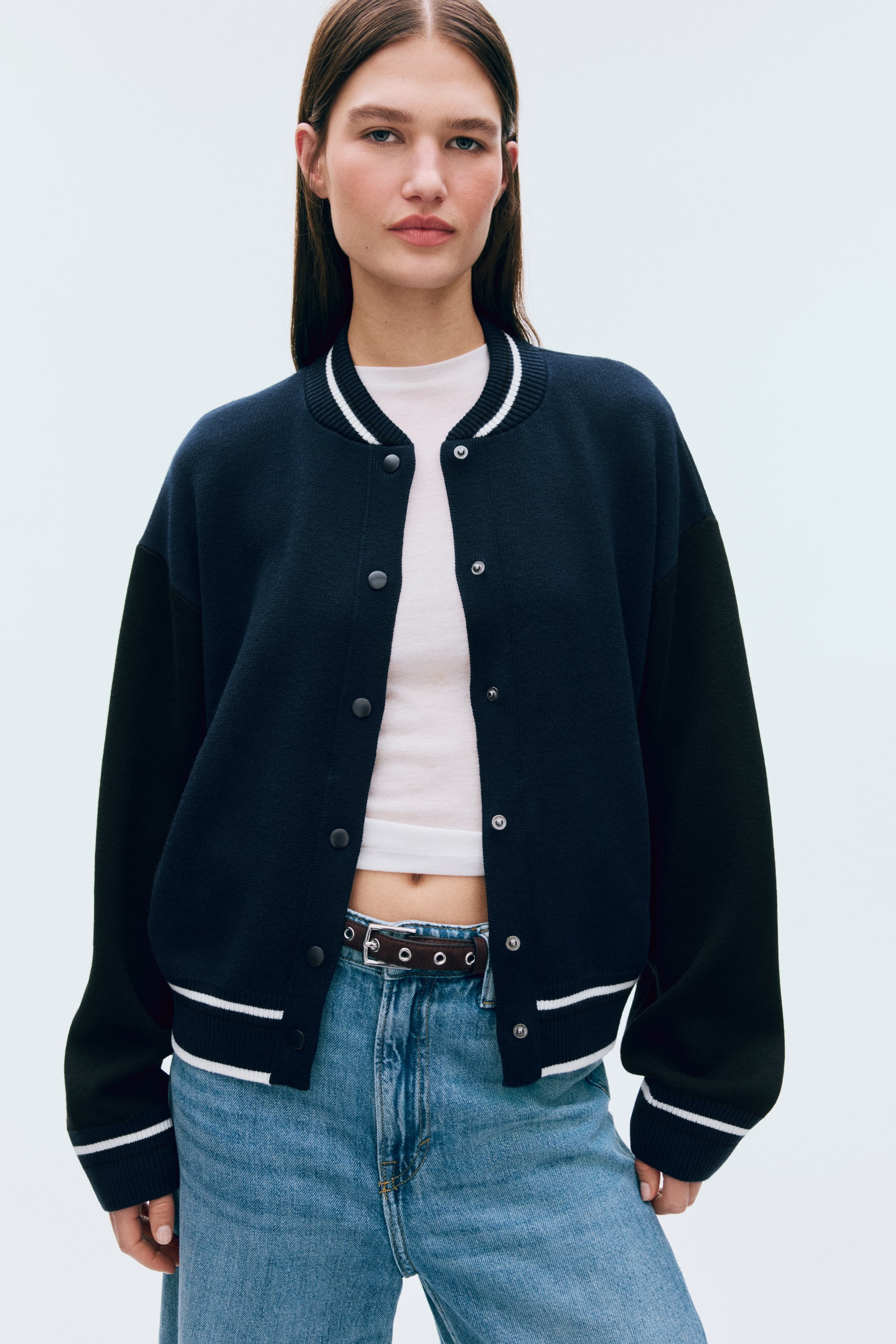 View larger image: Front-facing navy blue bomber jacket with black sleeves. It features a ribbed collar, cuffs, and hem detailed with white double stripes, and is styled open with snap buttons down the front.