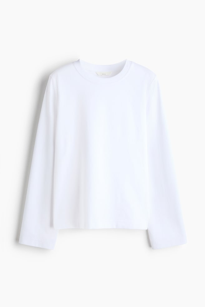A white cotton jersey top is shown from the front, featuring a round, rib-trimmed neckline and long, straight sleeves. The garment is hanging flat, showing a relaxed fit and a clean, straight hem. - 1