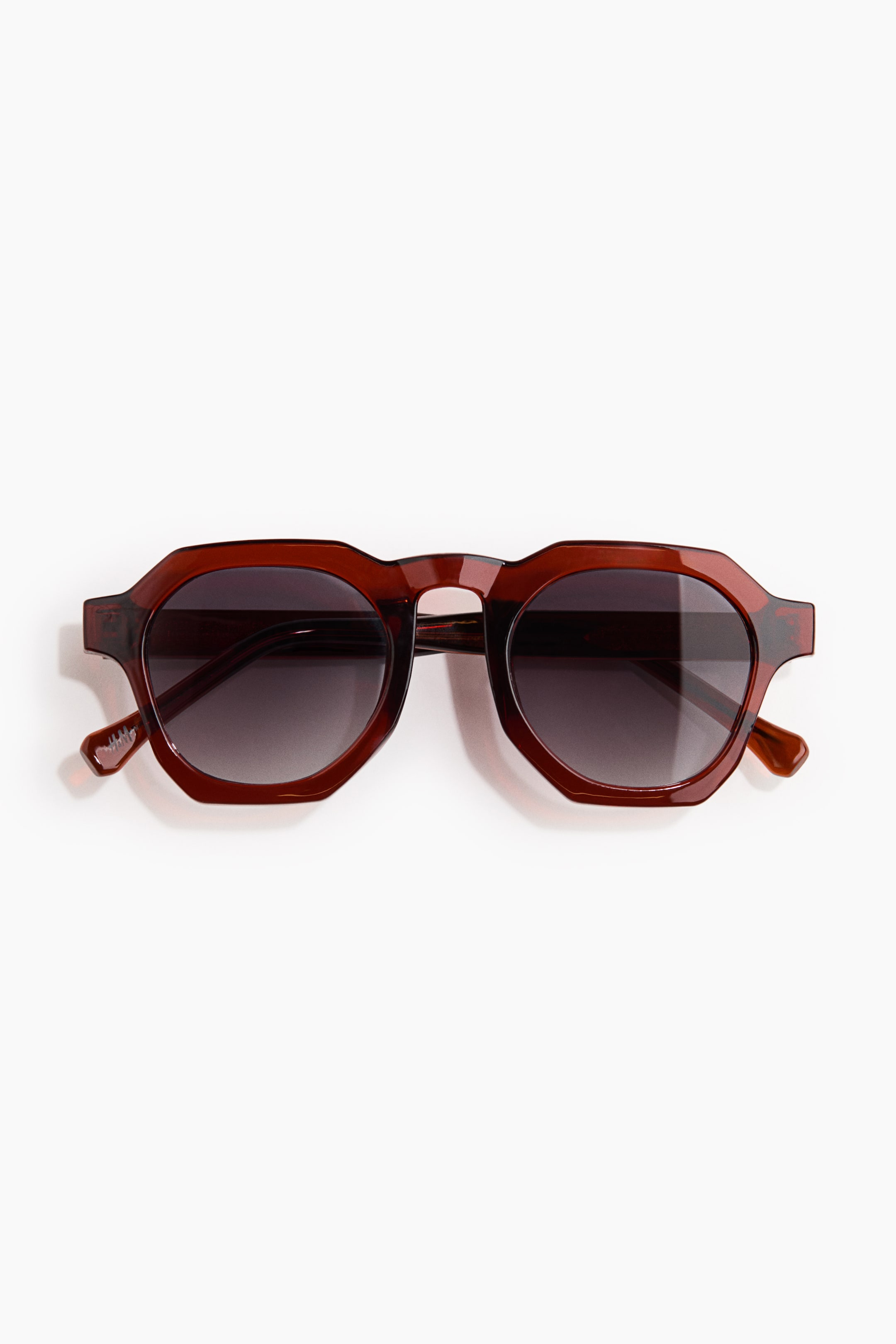 View larger image: Sunglasses are showcasing translucent brown frames with a geometric hexagonal shape and a keyhole bridge. Dark gradient lenses are enhancing the frame, and the temples are in harmony with the frame colour.