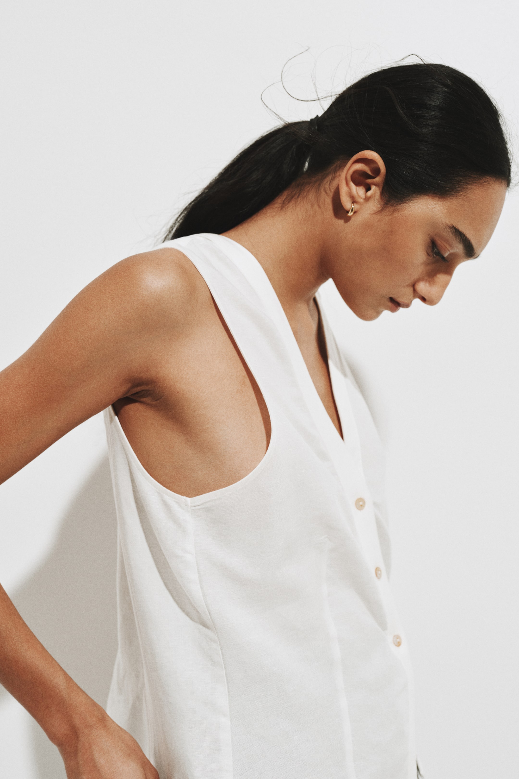 View larger image: A white sleeveless top made from a lightweight, textured fabric features a V-neckline and a button-down front, viewed from a slight side angle. Light-colored buttons are visible along the placket of the relaxed garment.