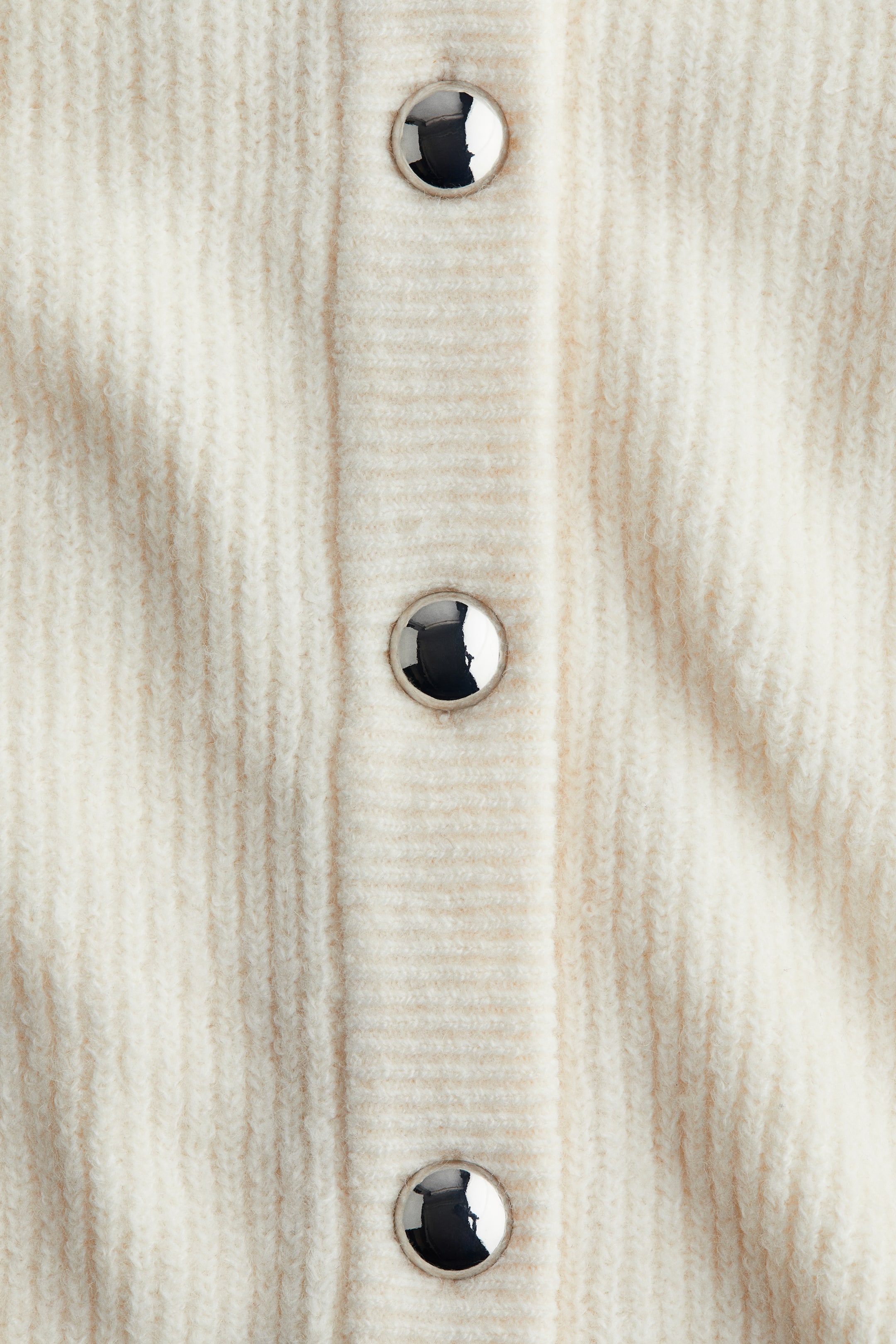 Zobacz większy obraz: Kremowy dzianinowy ubiór prezentuje swój przód, szczegółowo opisany wyraźną prążkowaną fakturą na całej powierzchni. Pionowa prążkowana plisa biegnie w dół środka, z trzema okrągłymi, błyszczącymi guzikami w srebrnym odcieniu, równomiernie rozmieszczonymi.