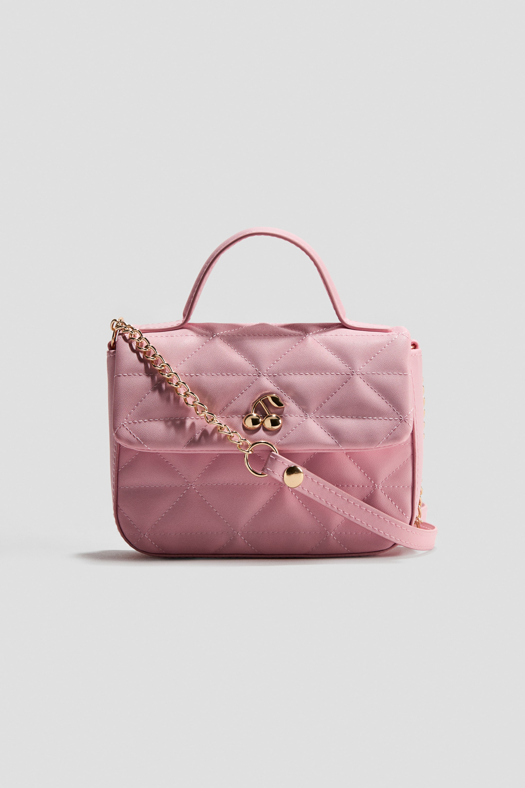 Ampliar la imagen: Bolsa de hombro acolchada. El frente de esta bolsa rosa muestra un patrón de acolchado en forma de diamante a lo largo de su cuerpo y solapa, con un único asa superior y un broche en forma de cereza en tono dorado. Una cadena en tono dorado a juego está conectada al lado, y una correa ajustable rosa se extiende desde la parte inferior derecha.