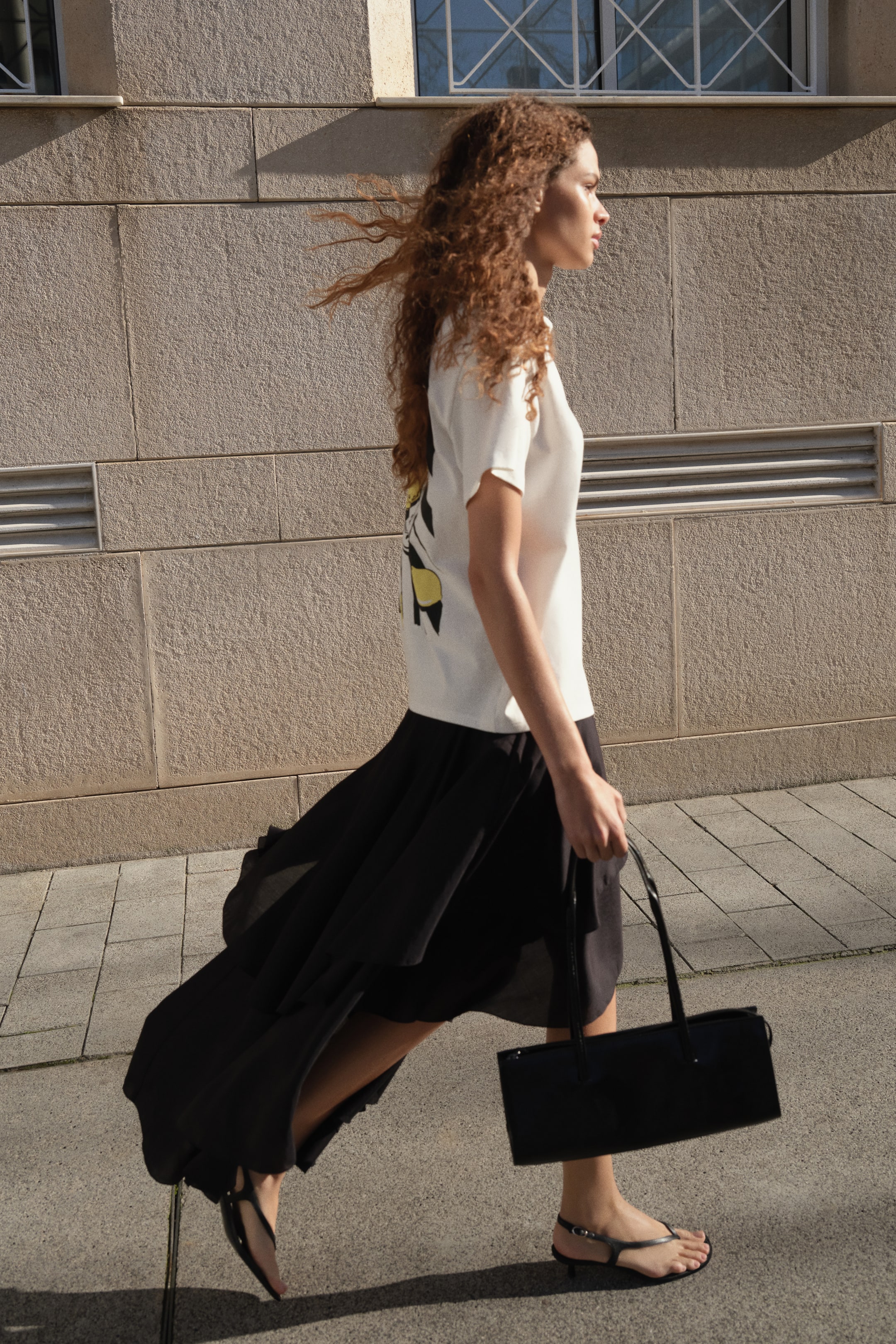 View larger image: A black rectangular handbag is being held horizontally by its two thin top handles. Its structured side profile is facing forward, showcasing its elongated shape.