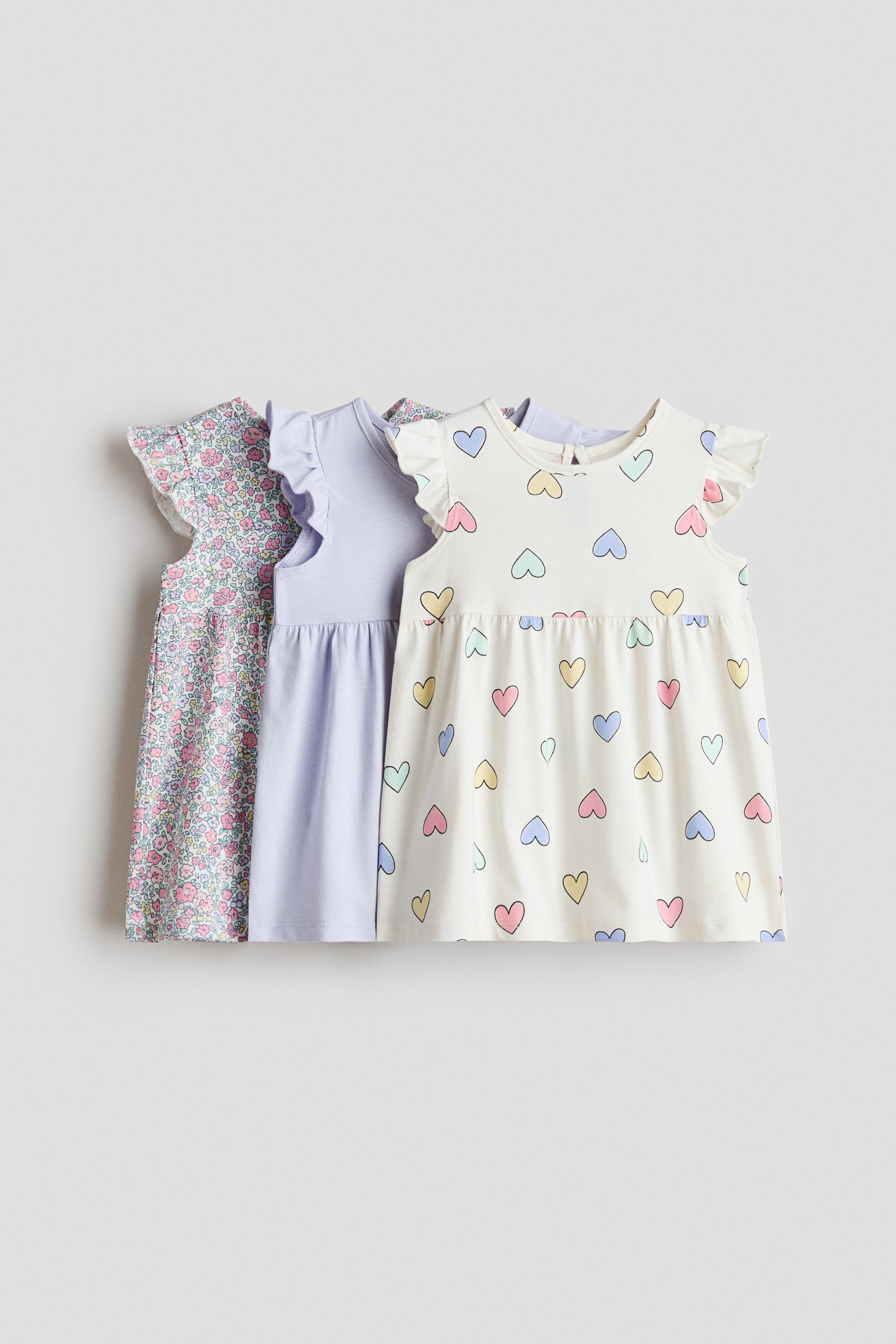 View larger image: Three dresses made from soft cotton jersey stand side by side, facing forward to showcase their diverse designs. They feature round, trimmed necklines, flutter sleeves, gathered waists, and flared skirts.