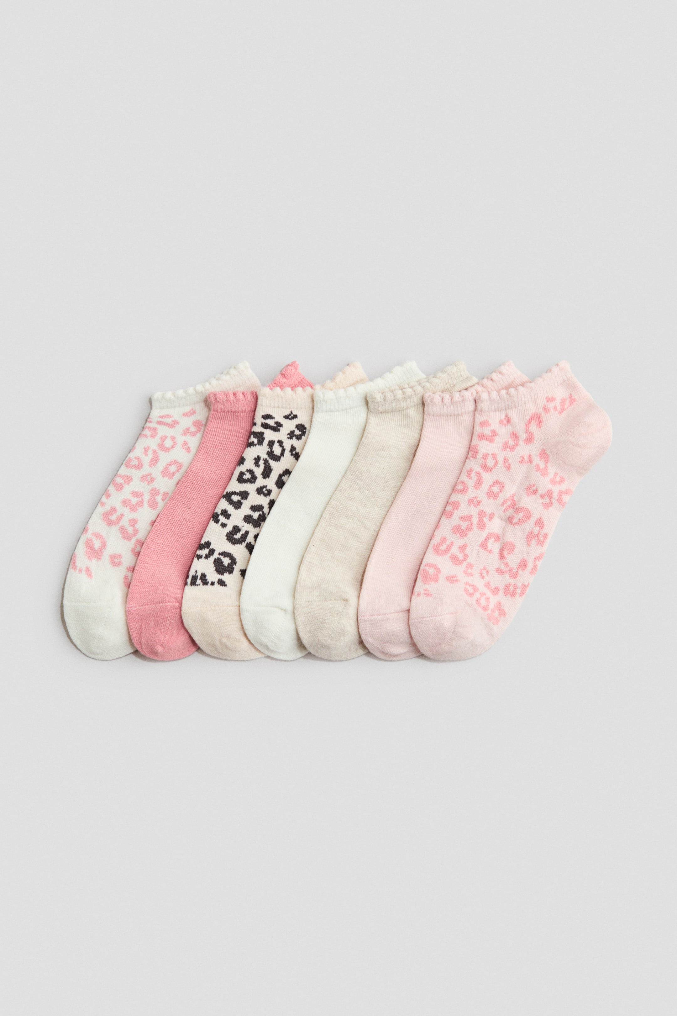 View larger image: "Seven fine-knit trainer socks are arranged in a neat row, angled towards the front. They boast elastication around the tops and display a variety of solid light pink, medium pink, off-white, and light beige shades, complemented by white and light pink socks adorned with leopard print patterns."