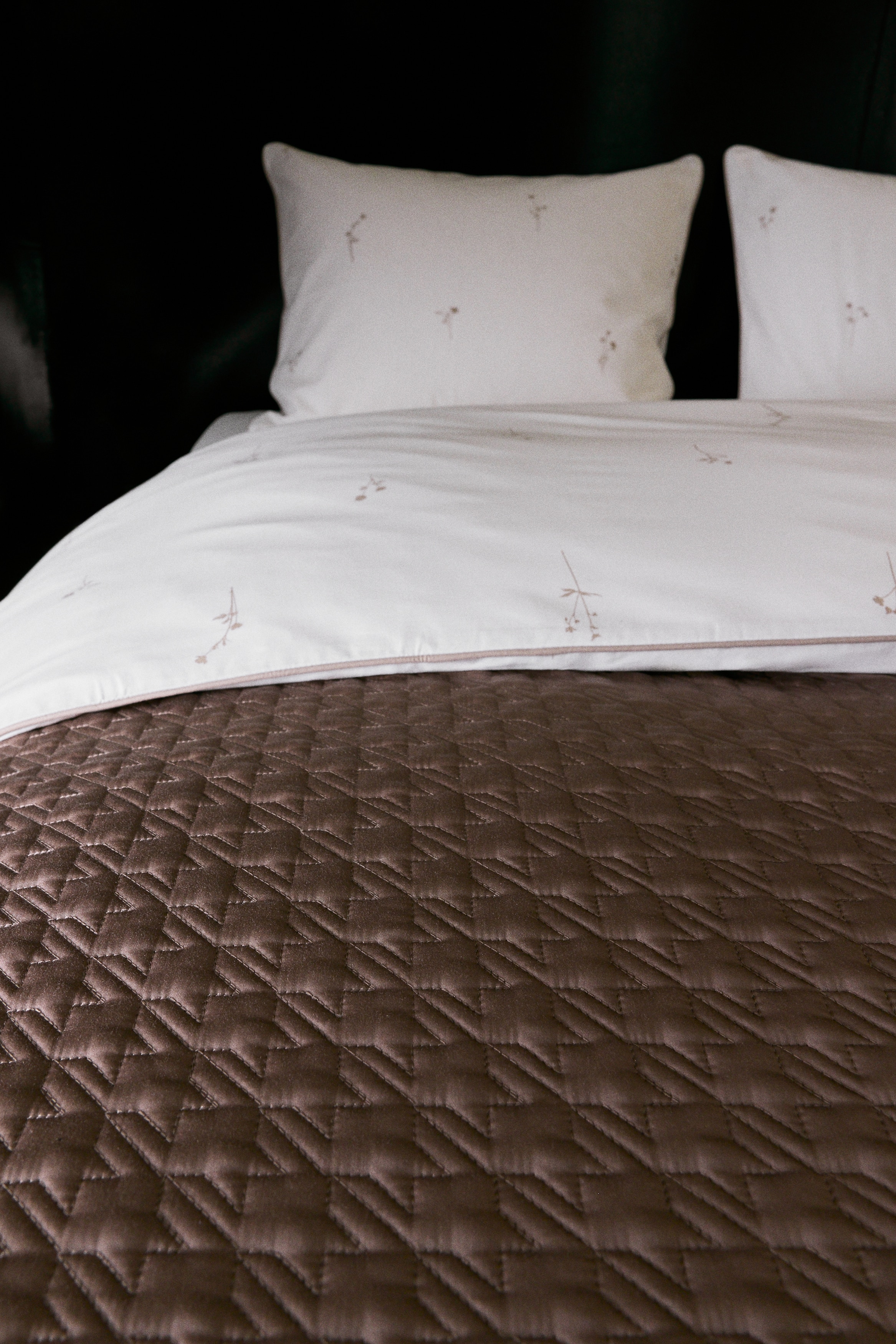 A quilted blanket features a repeated geometric pattern across its central area. A smooth, unquilted border surrounds all edges of the blanket.