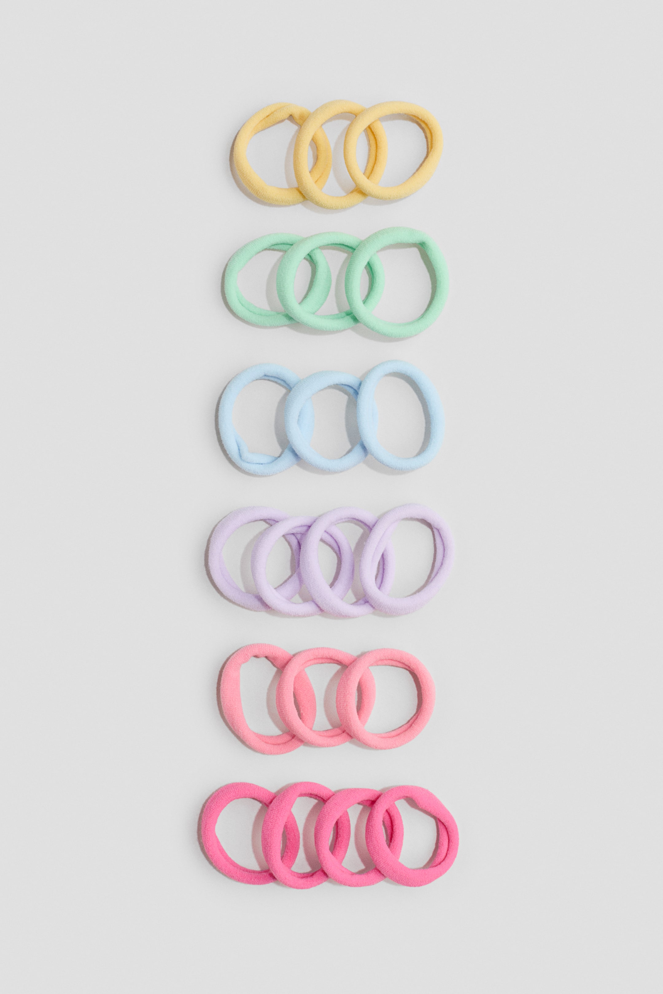 Agrandir l'image: Les élastiques à cheveux en jersey sont disposés en six rangées horizontales, avec trois élastiques par rangée. Ils présentent une texture douce recouverte de tissu et sont proposés en jaune, vert menthe, bleu clair, lavande, rose clair et rose fuchsia, sans attaches métalliques.