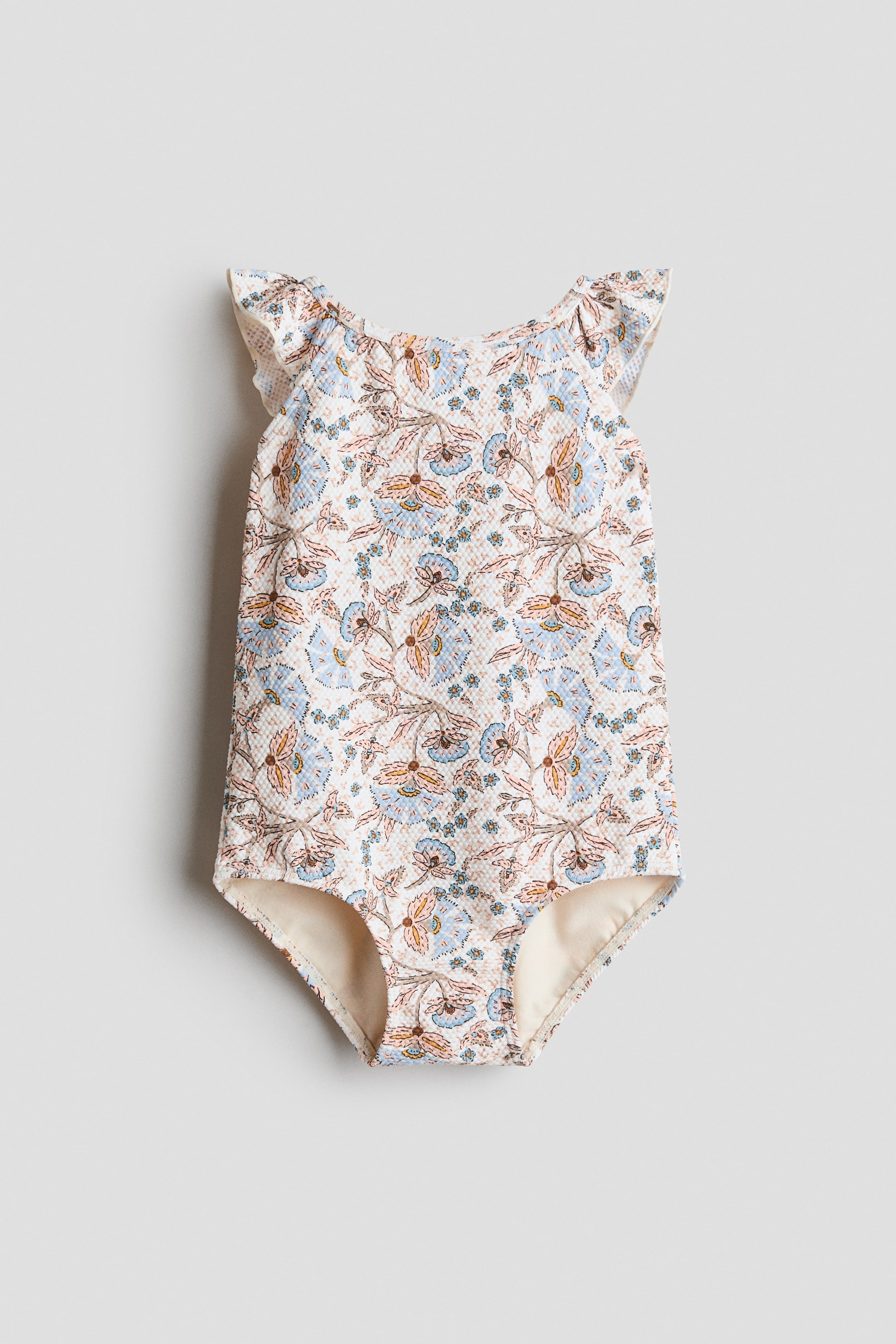 Grösseres Bild ansehen: Der H&M Adorables Badeanzug präsentiert sich von vorne und besticht durch einen strukturierten Stoff mit einem komplexen Blumenmuster in Hellblau, Braun und Creme. Er ist mit einem quadratischen Ausschnitt und Rüschen-Trägern gestaltet, die mit Overlock-Nähten abgeschlossen sind.