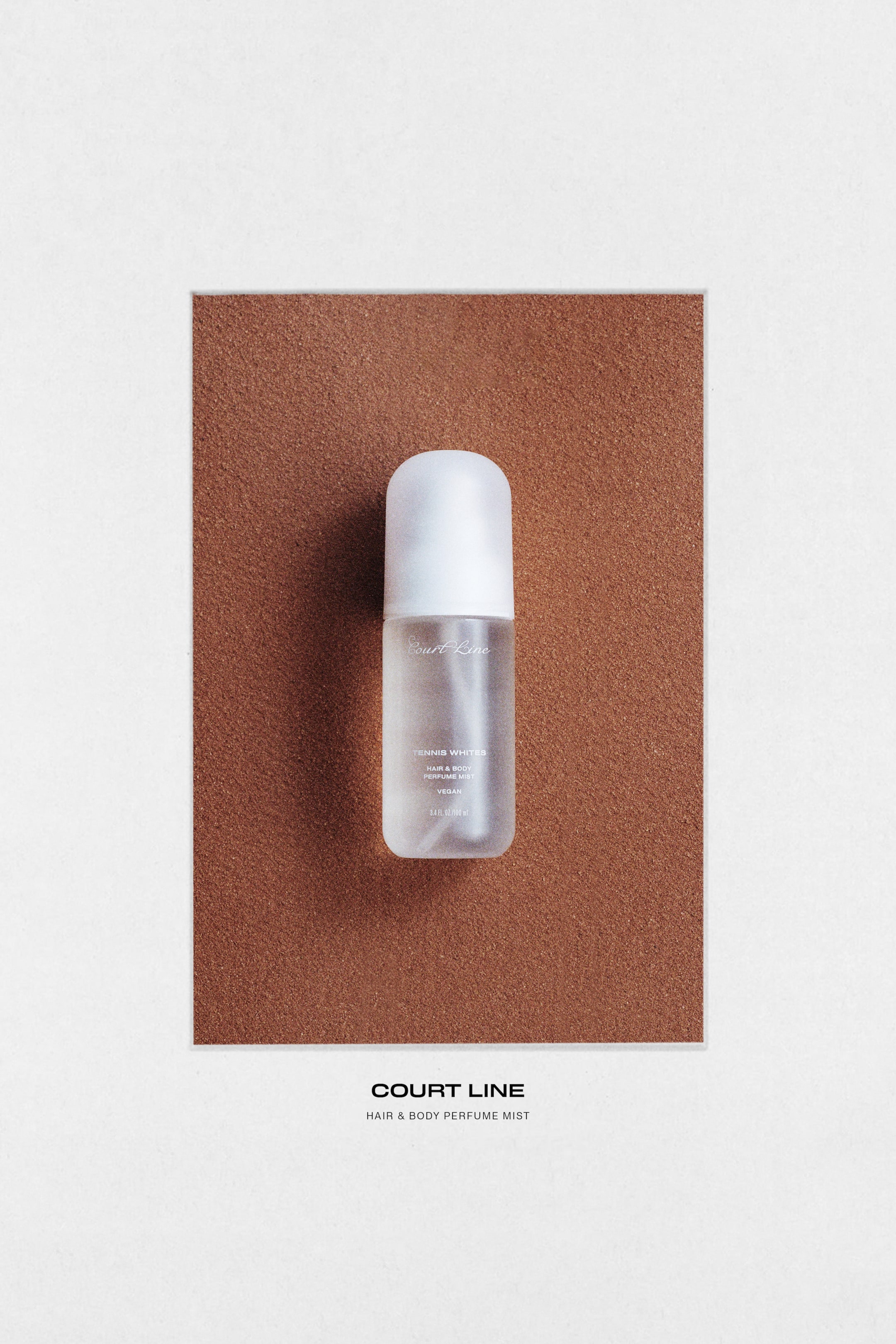 View larger image: The Court Line hair & body perfume mist is presented in a rounded cylindrical frosted bottle containing a clear liquid, topped with an opaque white rounded cap. The front label showcases the brand name, "Tennis Whites," "Hair & Body Perfume Mist," and "Vegan" in dark text.