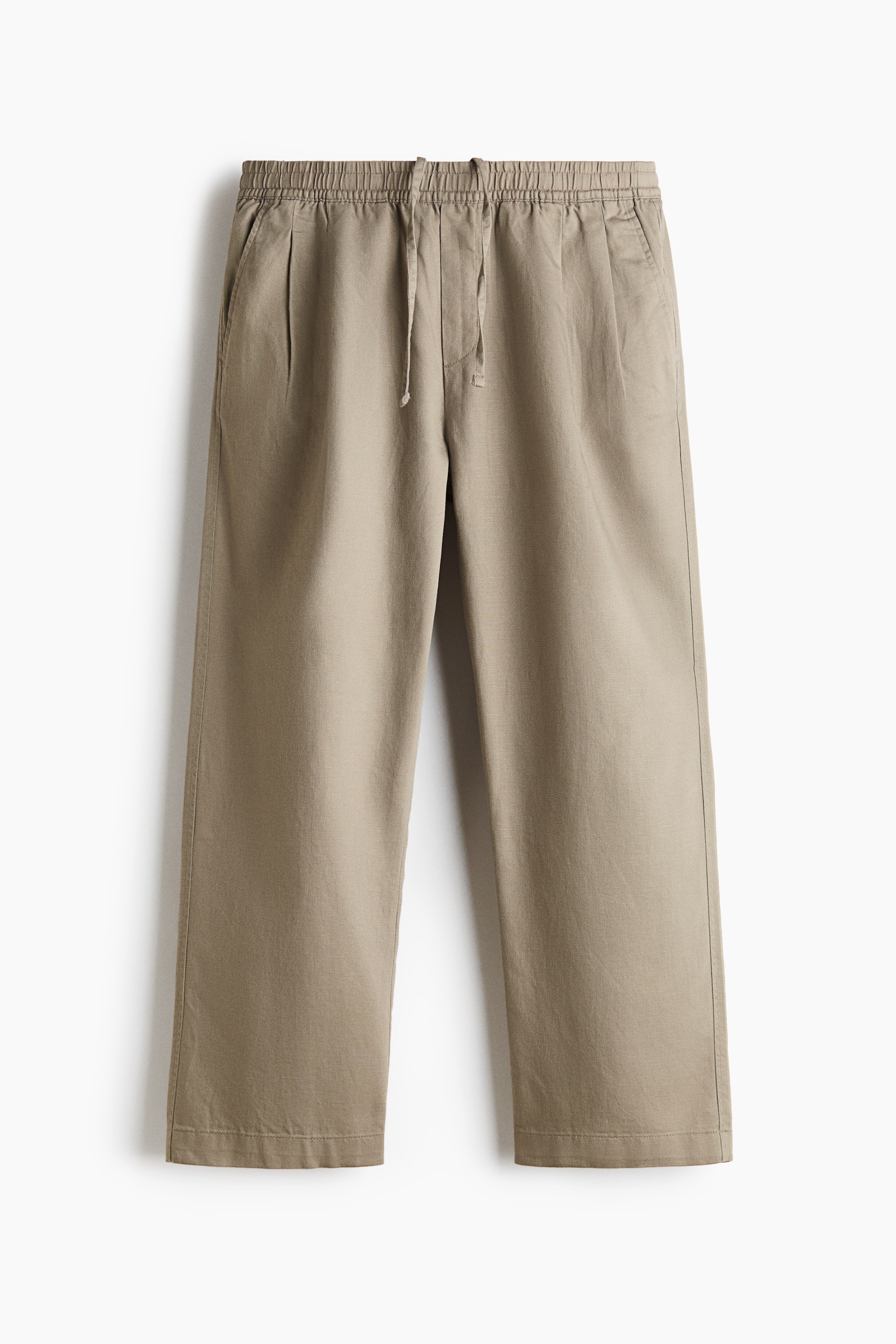View larger image: A pair of beige trousers is hanging facing front, showing an elasticated waistband with a matching drawstring, a faux fly, and diagonal side pockets. The trousers feature straight legs with subtle front pleats and a relaxed silhouette.