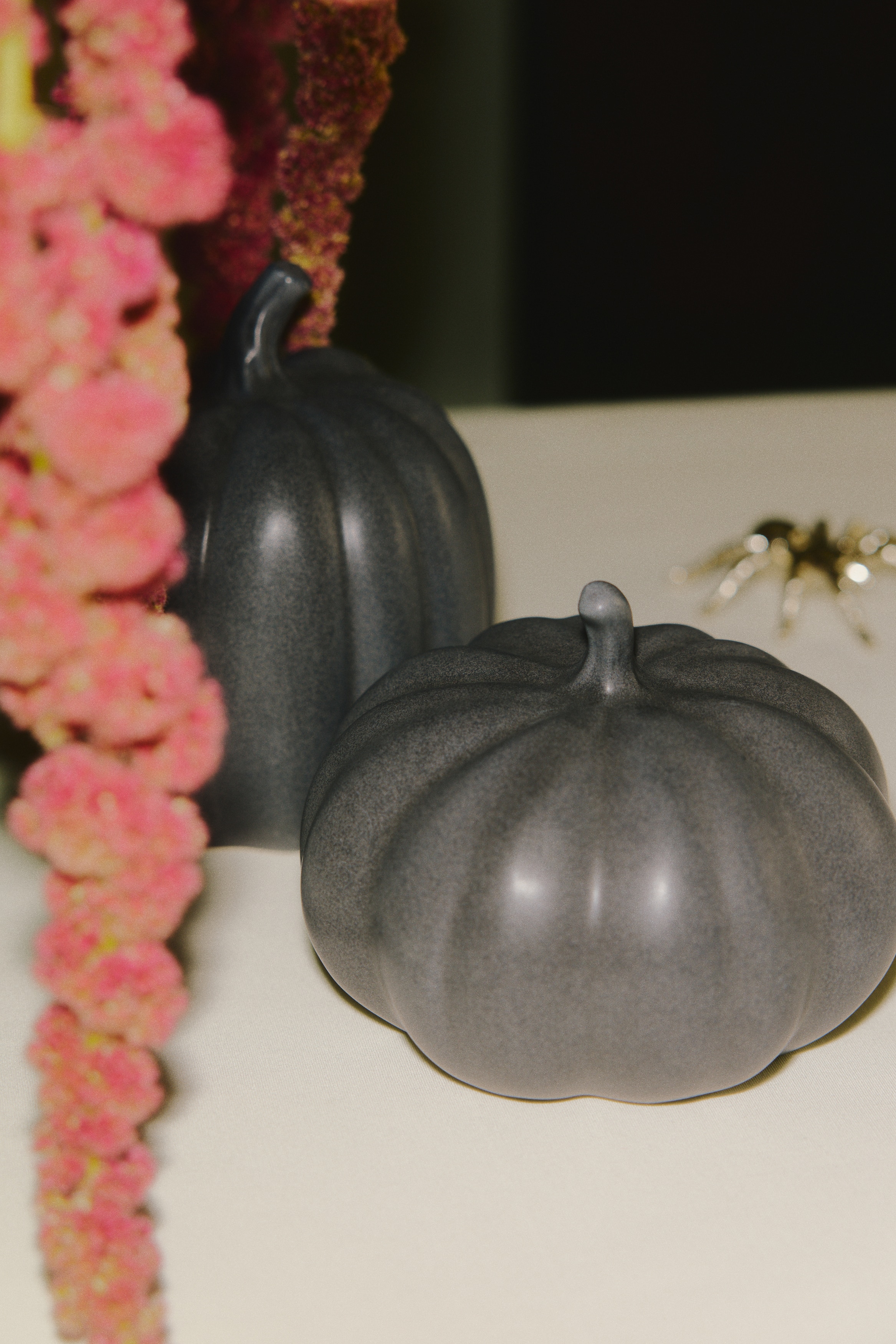 A pumpkin-shaped stoneware ornament features a dark grey, speckled surface with distinct vertical ribs and a short, curved stem.