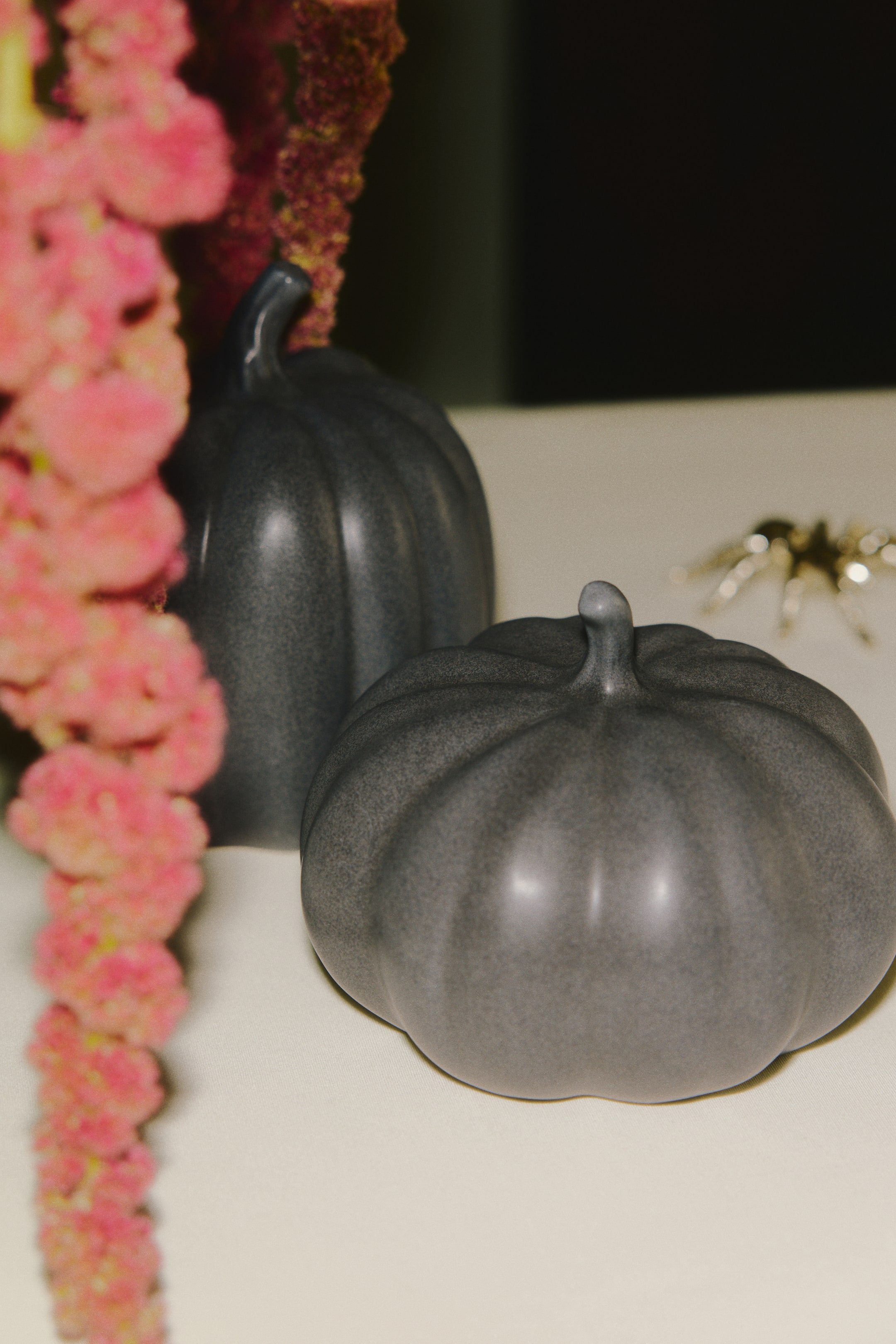 View larger image: Two dark grey stoneware pumpkin-shaped decorations are sitting on a surface, showcasing a ribbed design and a small stem at the top. The foreground pumpkin is broad and squat, while the background pumpkin is taller and narrower.