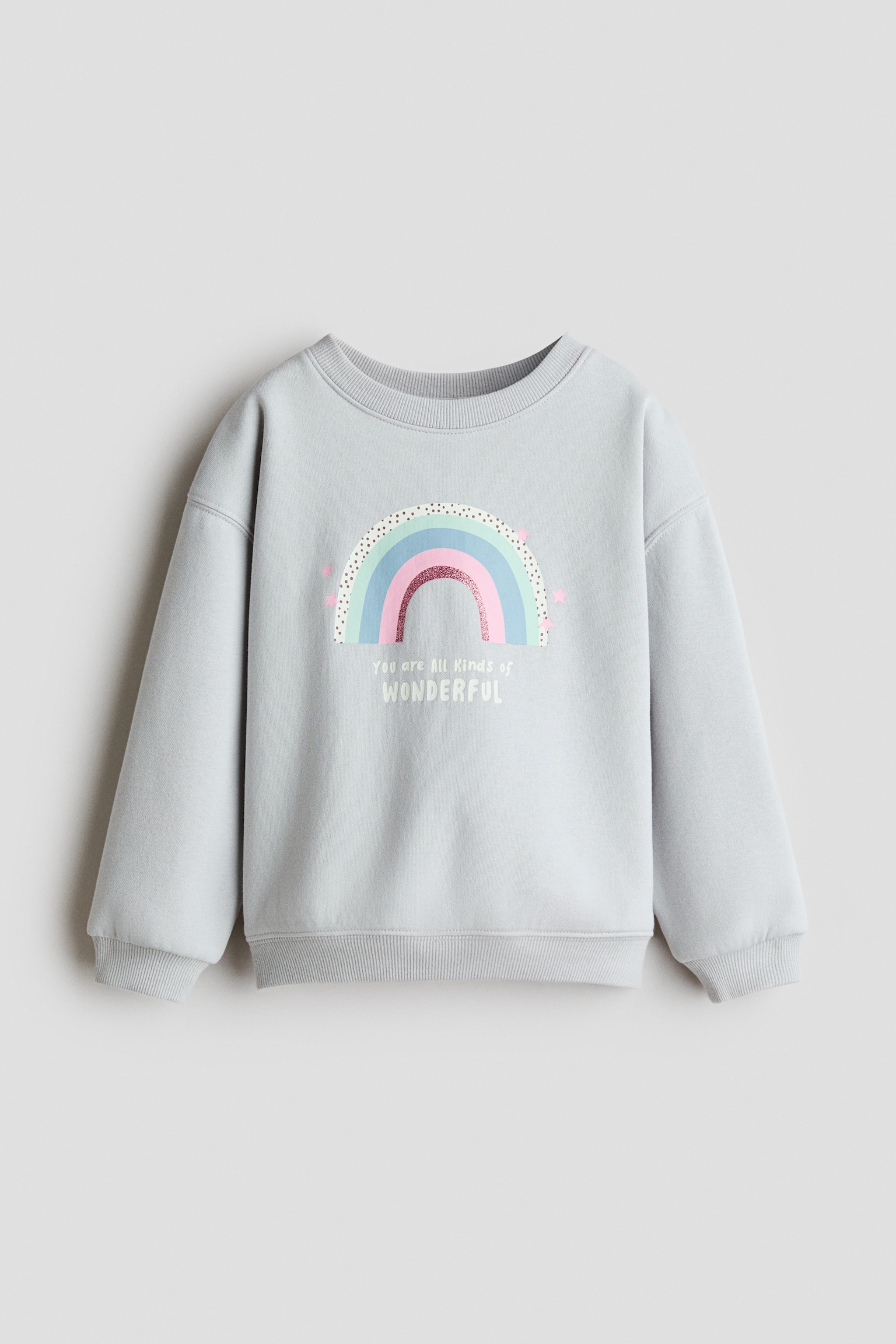 A light grey sweatshirt is shown from the front, featuring a pastel rainbow graphic and the text "You are All kinds of WONDERFUL" printed on the chest. It is constructed with a ribbed crew neck, dropped shoulders, and ribbed cuffs and hem.