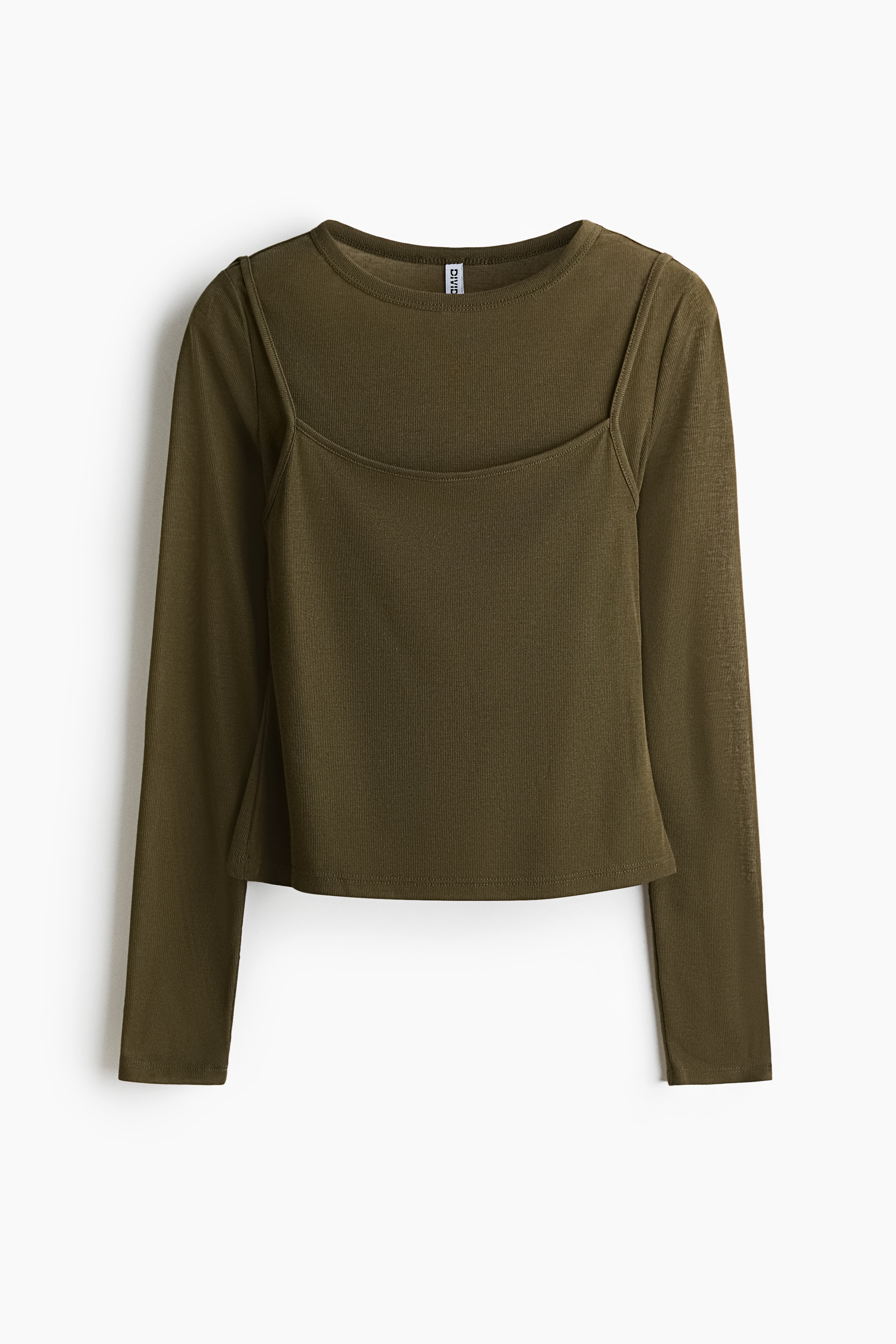 A long-sleeve, fitted olive green top in narrow ribbed jersey, featuring a layered design with a scoop-neck outer layer, is being worn and lightly adjusted at the shoulder by the model. The top is styled with light-wash, wide-leg denim shorts with frayed hems.