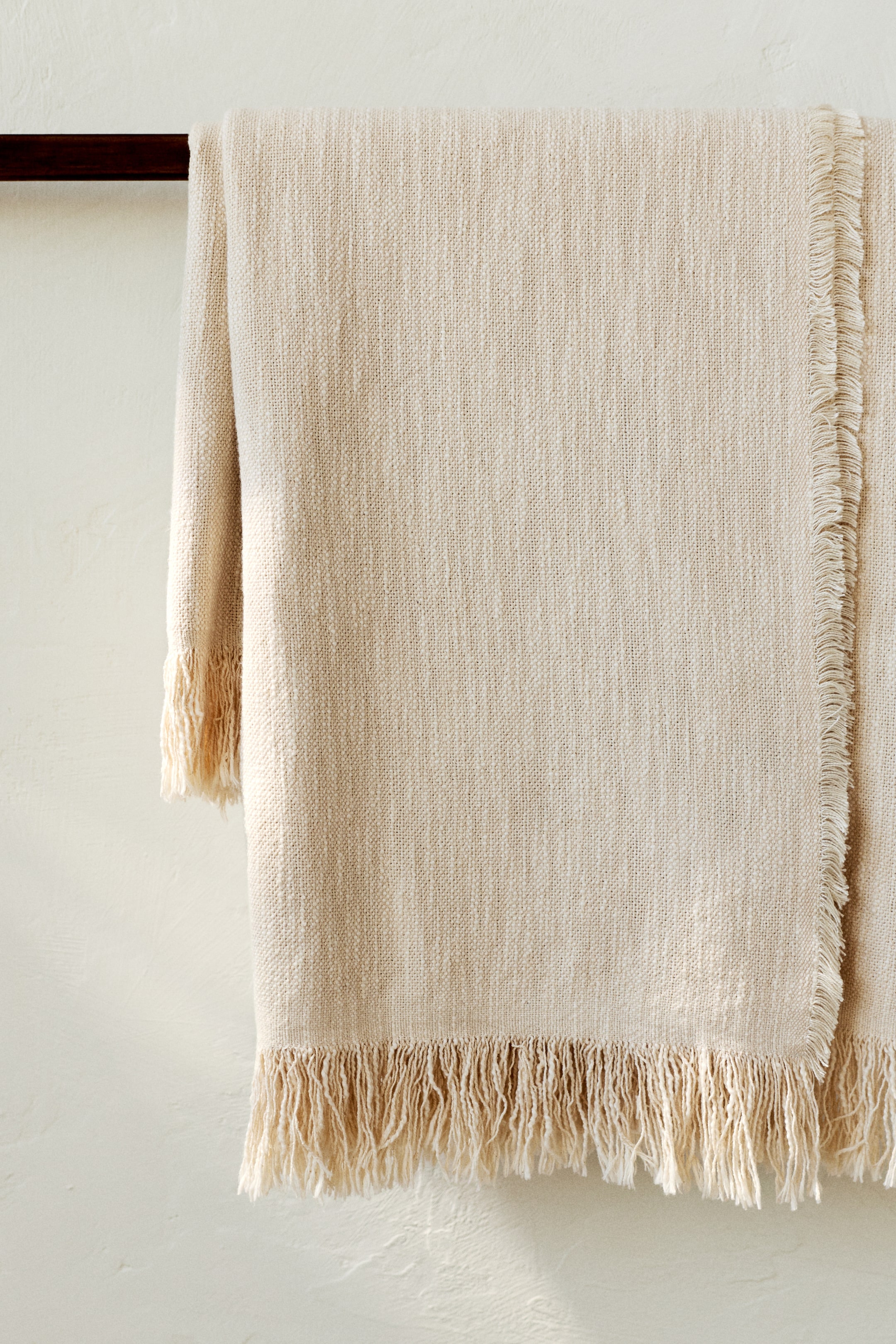 View larger image: A light beige woven blanket is draped, showcasing a textured weave and fringed edges along its bottom and right side.