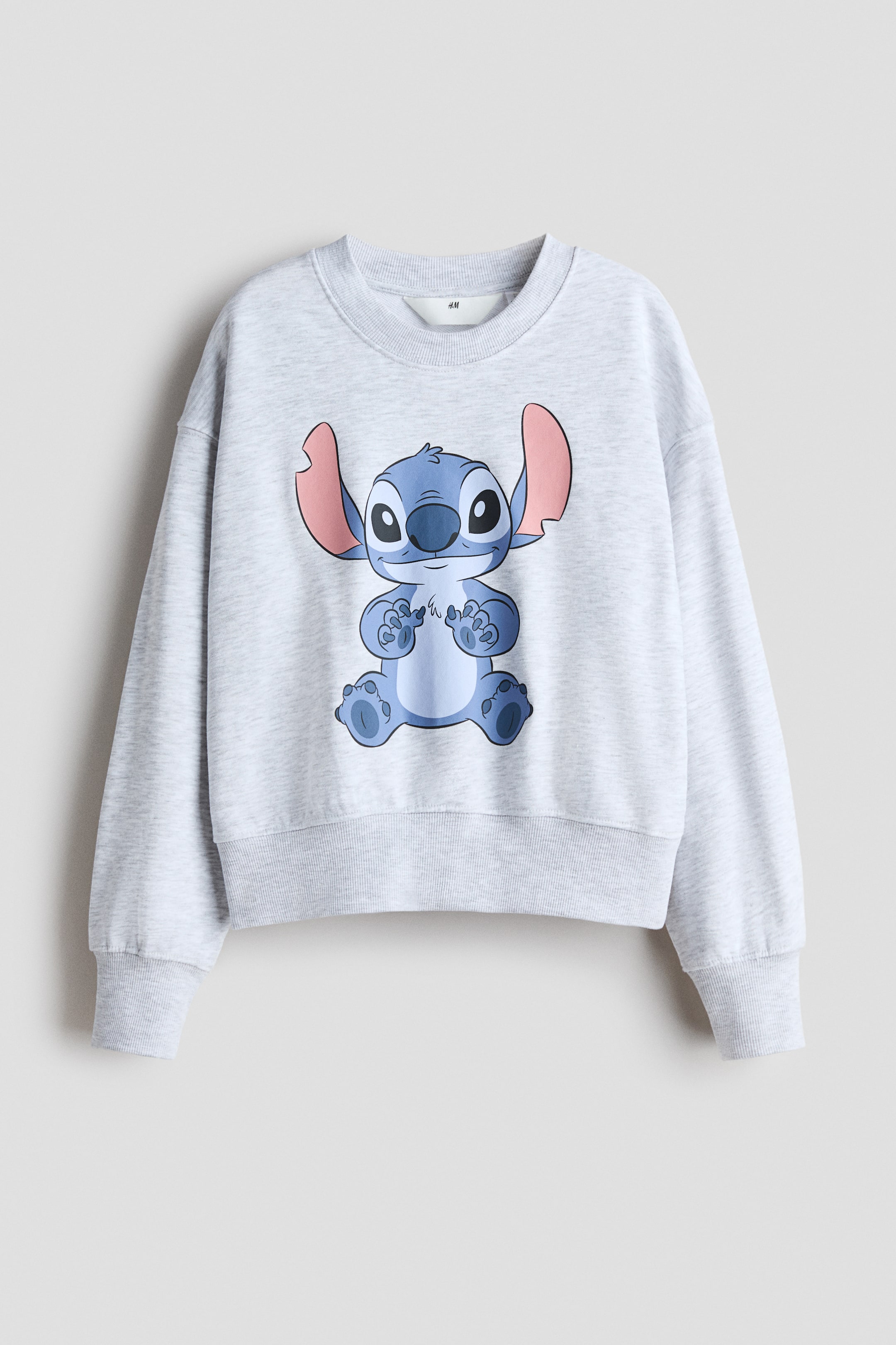 View larger image: An oversized top made of light gray sweatshirt fabric is presenting its front, featuring a blue cartoon character print with large pink ears on the chest. 