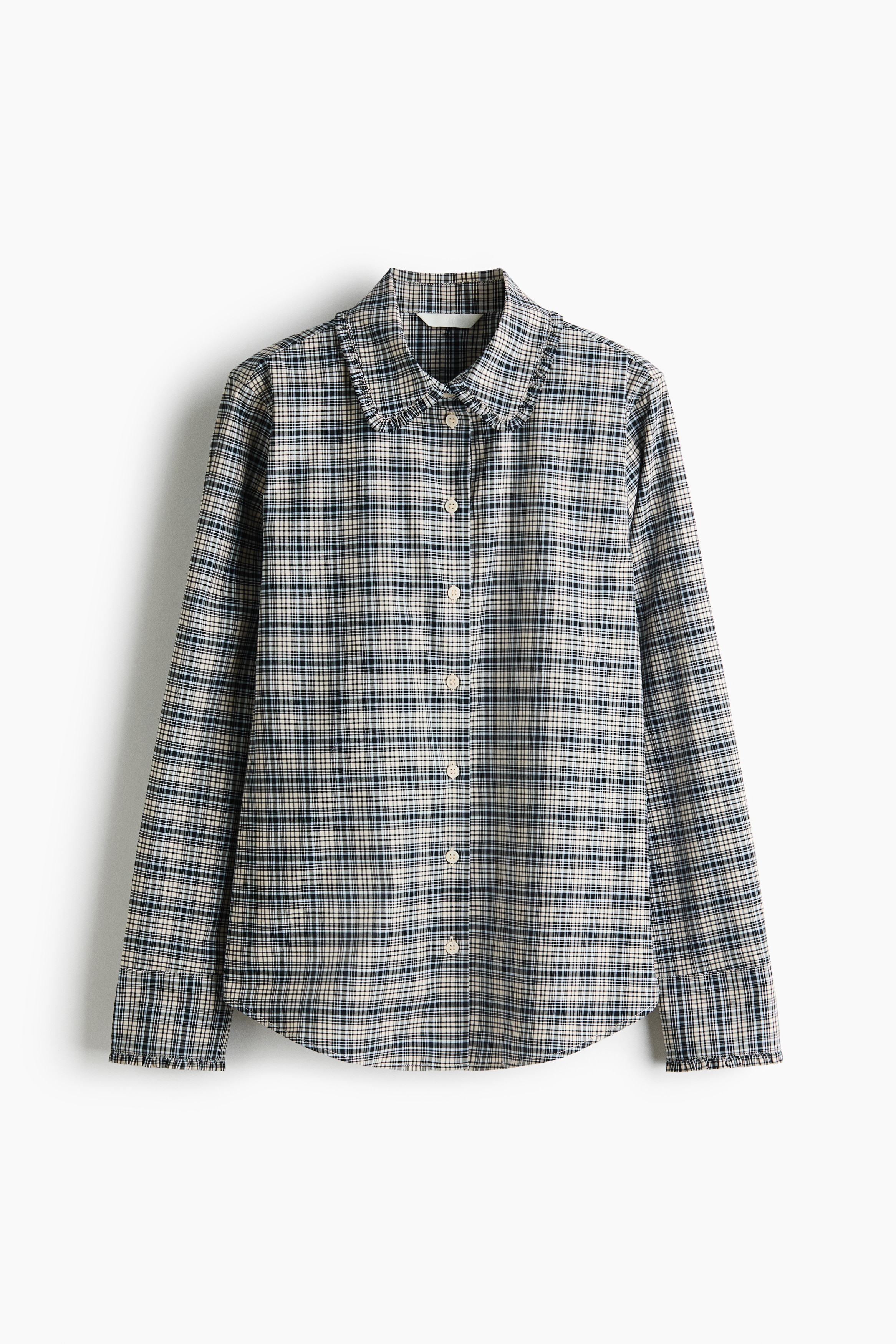 La modella indossa una camicia a quadri a maniche lunghe con colletto rifinito da volant, con i bottoni anteriori parzialmente slacciati e le maniche arrotolate. La camicia è abbinata a jeans in denim scuro e a un capo di colore blu acceso annodato in vita.