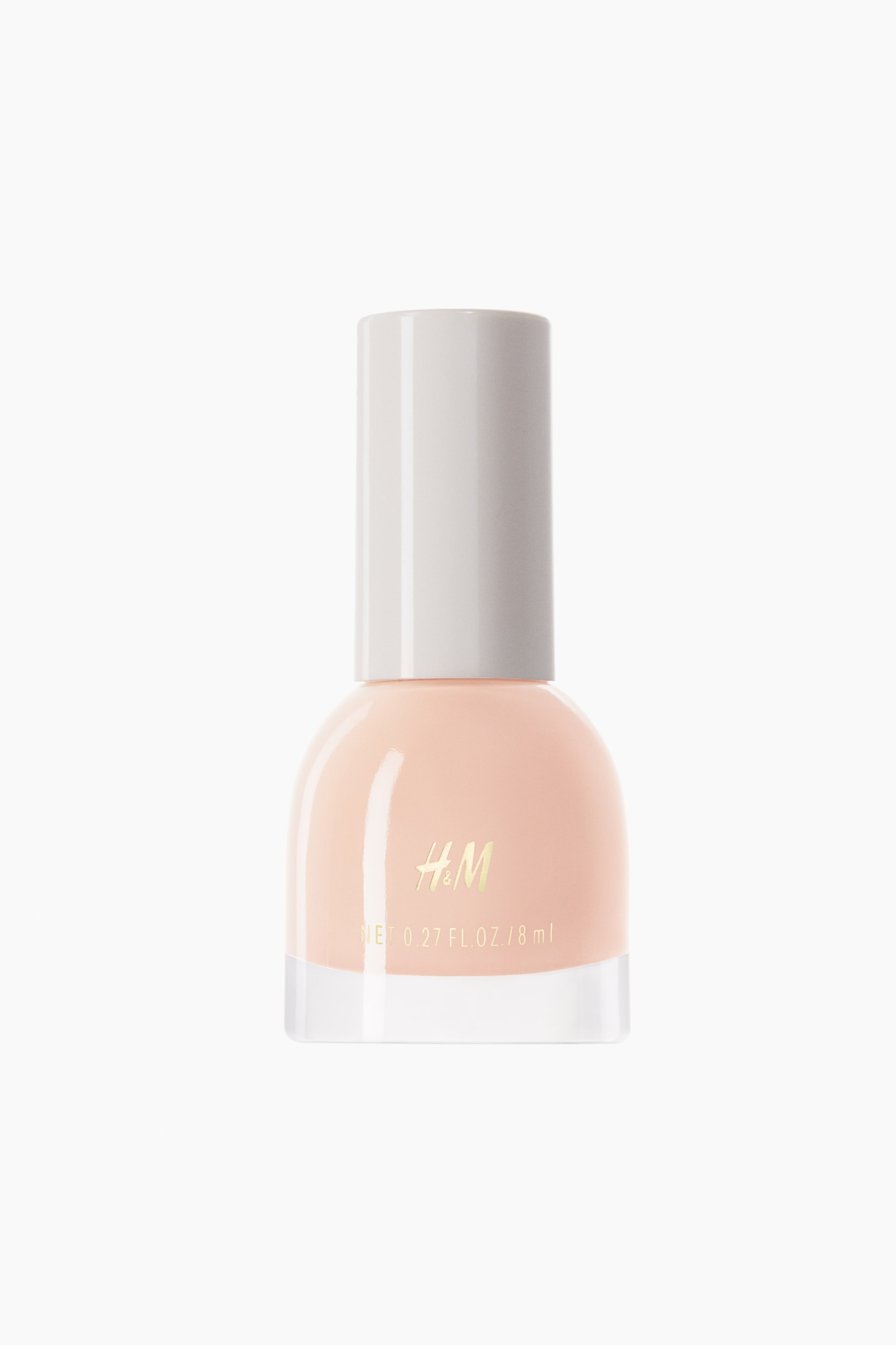 Agrandir l'image: Un flacon de vernis à ongles est présenté debout, de face, avec une bouteille ronde en verre transparent remplie d’un vernis pêche clair et surmontée d’un long bouchon cylindrique blanc. La face avant du flacon affiche le logo H&M ton doré ainsi que les indications de volume.
