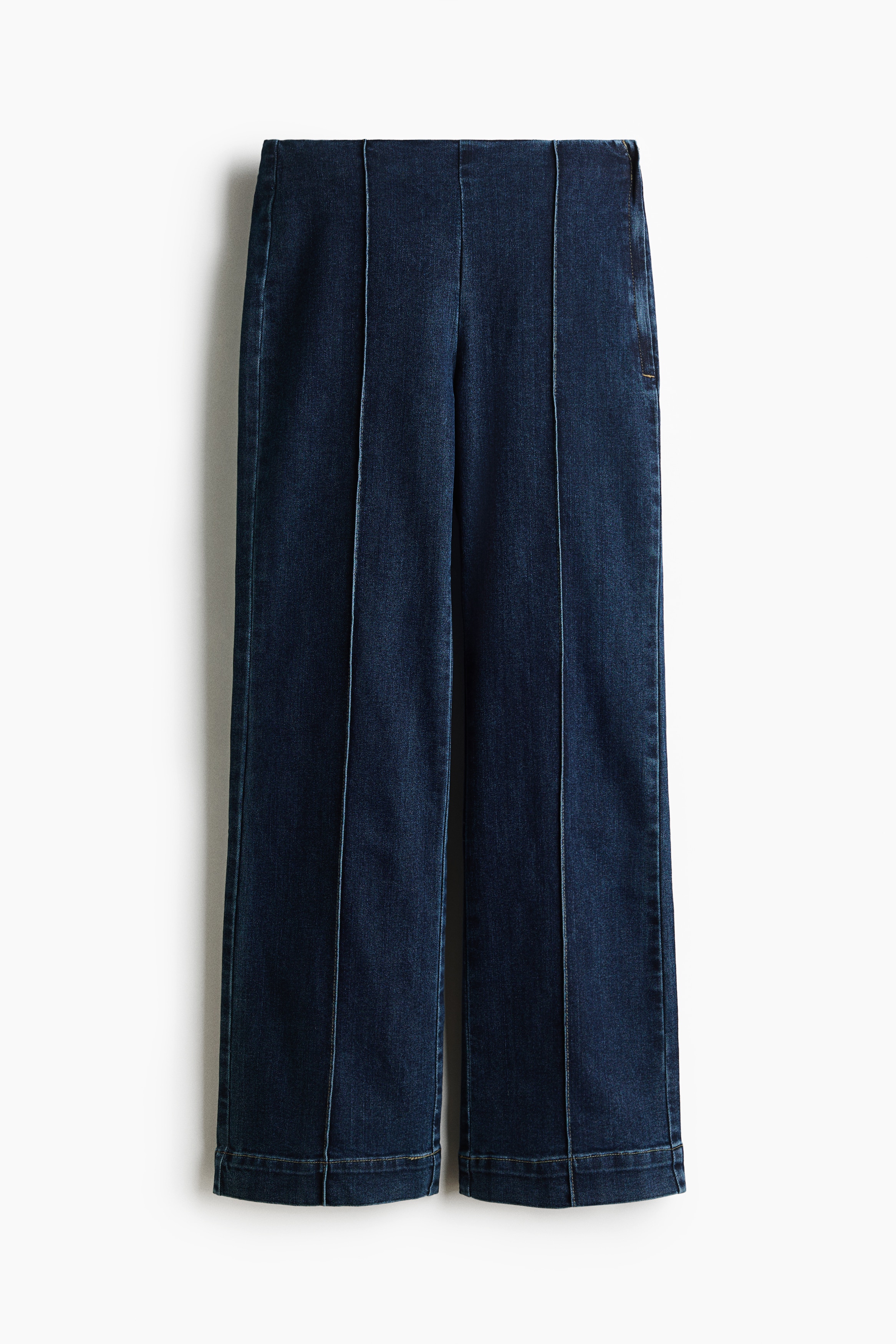 A pair of dark wash denim trousers is displayed from the front, featuring a high-rise waist and a wide-leg silhouette. Vertical stitched seams run down the centre of each leg, ending at wide, double-stitched hems.