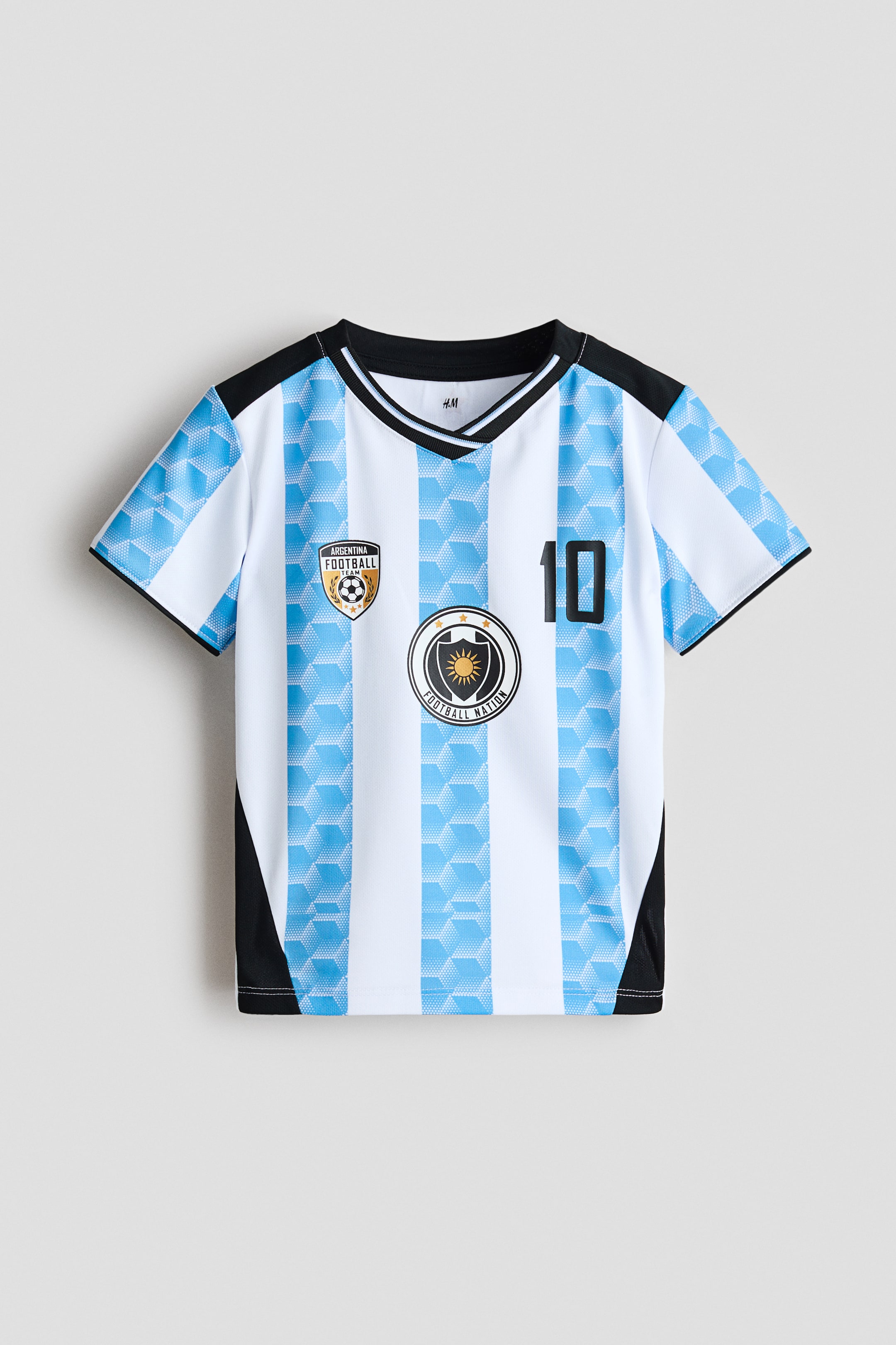Agrandir l'image: Un maillot de football à manches courtes en mesh imprimé présente un col en V noir à bordure côtelée avec une fine rayure blanche, vu de face. Il affiche des rayures verticales blanches et bleu clair, les rayures bleues présentant un motif de cubes géométriques, avec des panneaux noirs s'étendant des épaules le long des côtés. Un emblème est situé sur la poitrine gauche, et un autre emblème accompagné du numéro 10 se trouve sur la poitrine droite.
