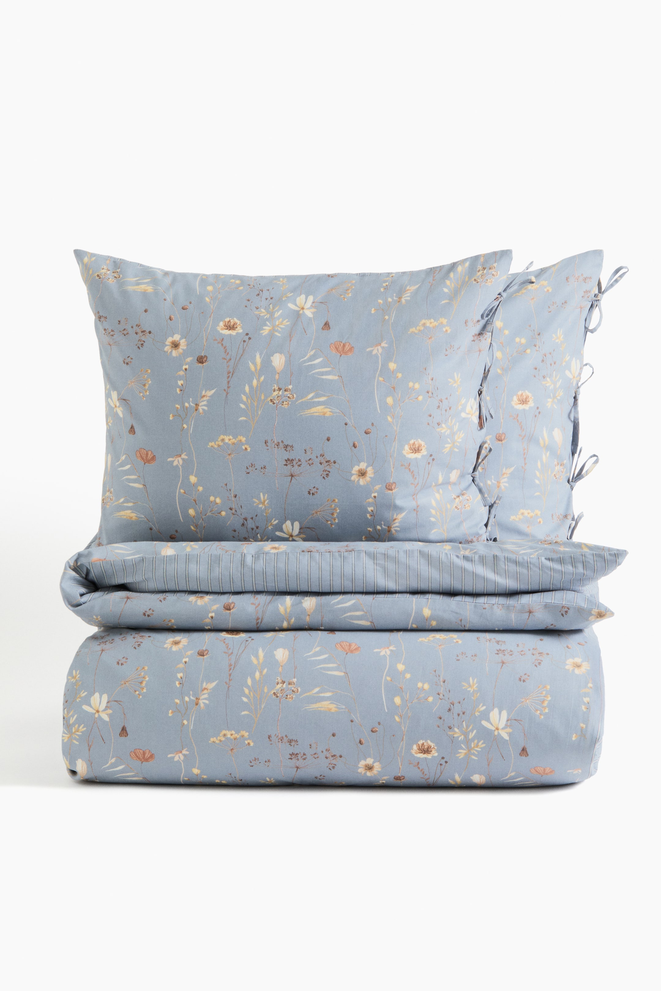 View larger image: A duvet cover set crafted in a soft cotton weave features a floral pattern on the front. The set, which includes one duvet cover and two matching pillowcases, showcases classic stripes on the reverse side of the duvet cover. The pillowcases are secured with ties on one side.