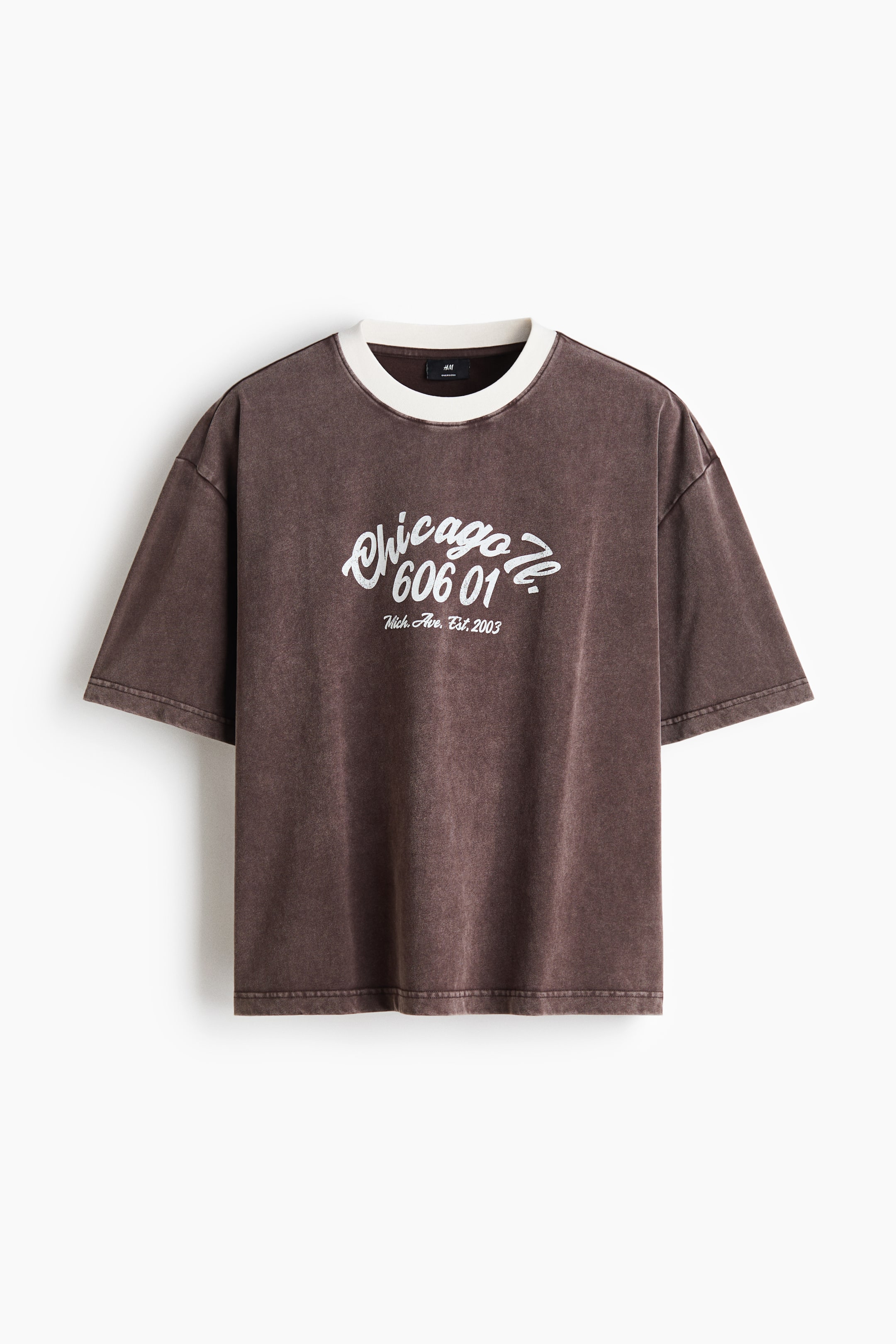View larger image: A brown oversized t-shirt is shown from the front, featuring a faded, garment-dyed wash, dropped shoulders, and wide sleeves. It has a contrasting white ribbed crew neck and a white graphic print on the chest with the text "Chicago Ill. 606 01."