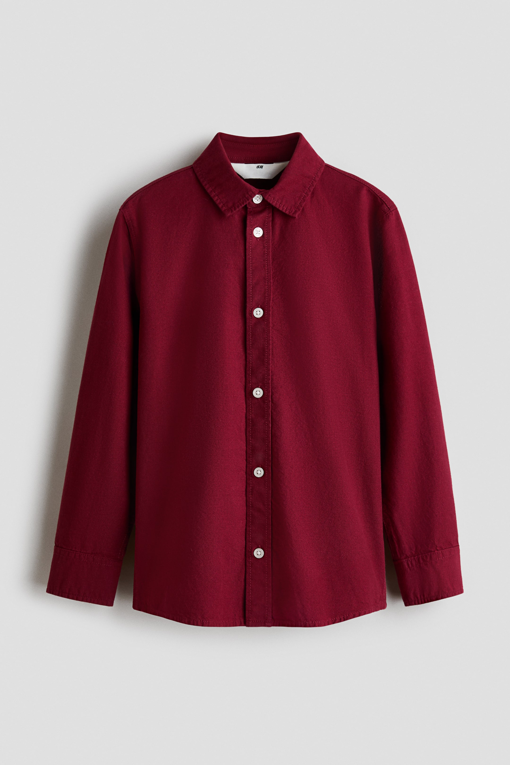 View larger image: A dark red, long-sleeved shirt in a soft cotton weave is presented from the front, featuring a turn-down collar, white buttons down the front, buttoned cuffs, and a rounded hem.