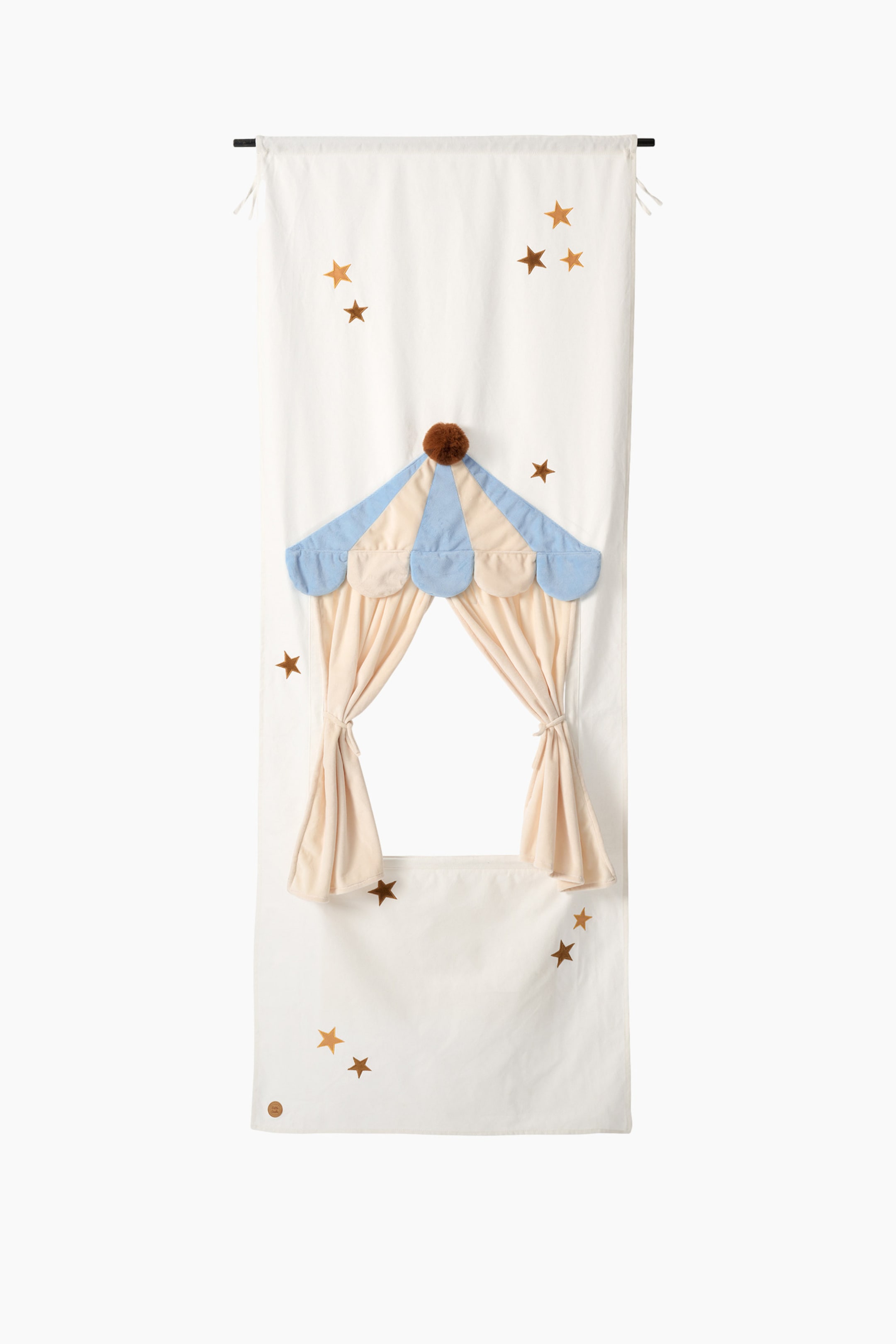 Agrandir l'image: Un rideau de porte de maisonnette en tissu crème est suspendu verticalement, avec un auvent festonné bleu et beige surmonté d'un pompon marron à son sommet. Des rideaux beiges sont attachés de chaque côté d'une ouverture centrale, et des étoiles dorées éparses décorent le tissu.