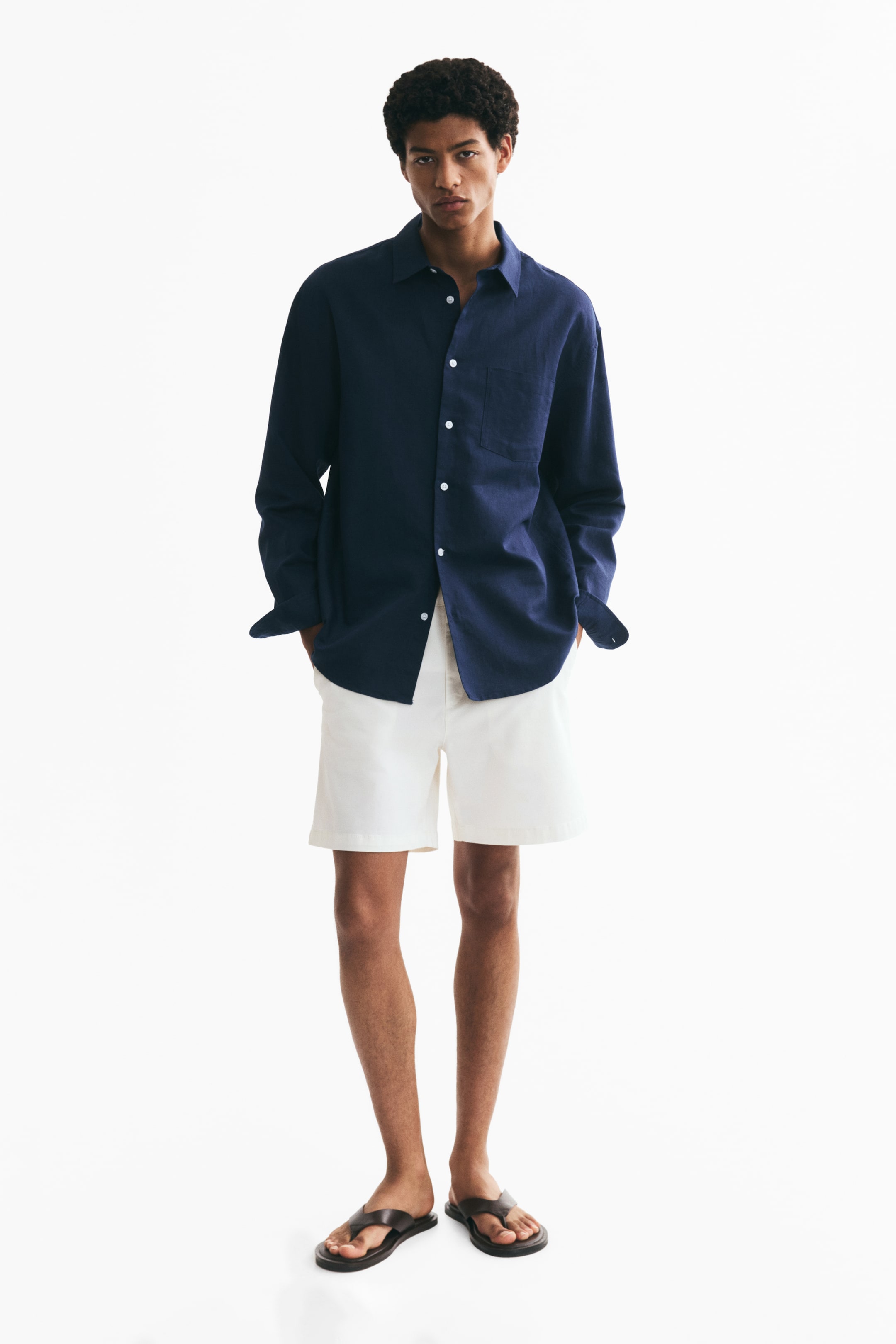 Xem ảnh lớn hơn: Quần short chino màu trắng dáng regular fit được người mẫu mặc, đang đứng với hai tay đặt trong túi chéo hai bên. Quần short được phối cùng áo sơ mi dài tay màu tối.
