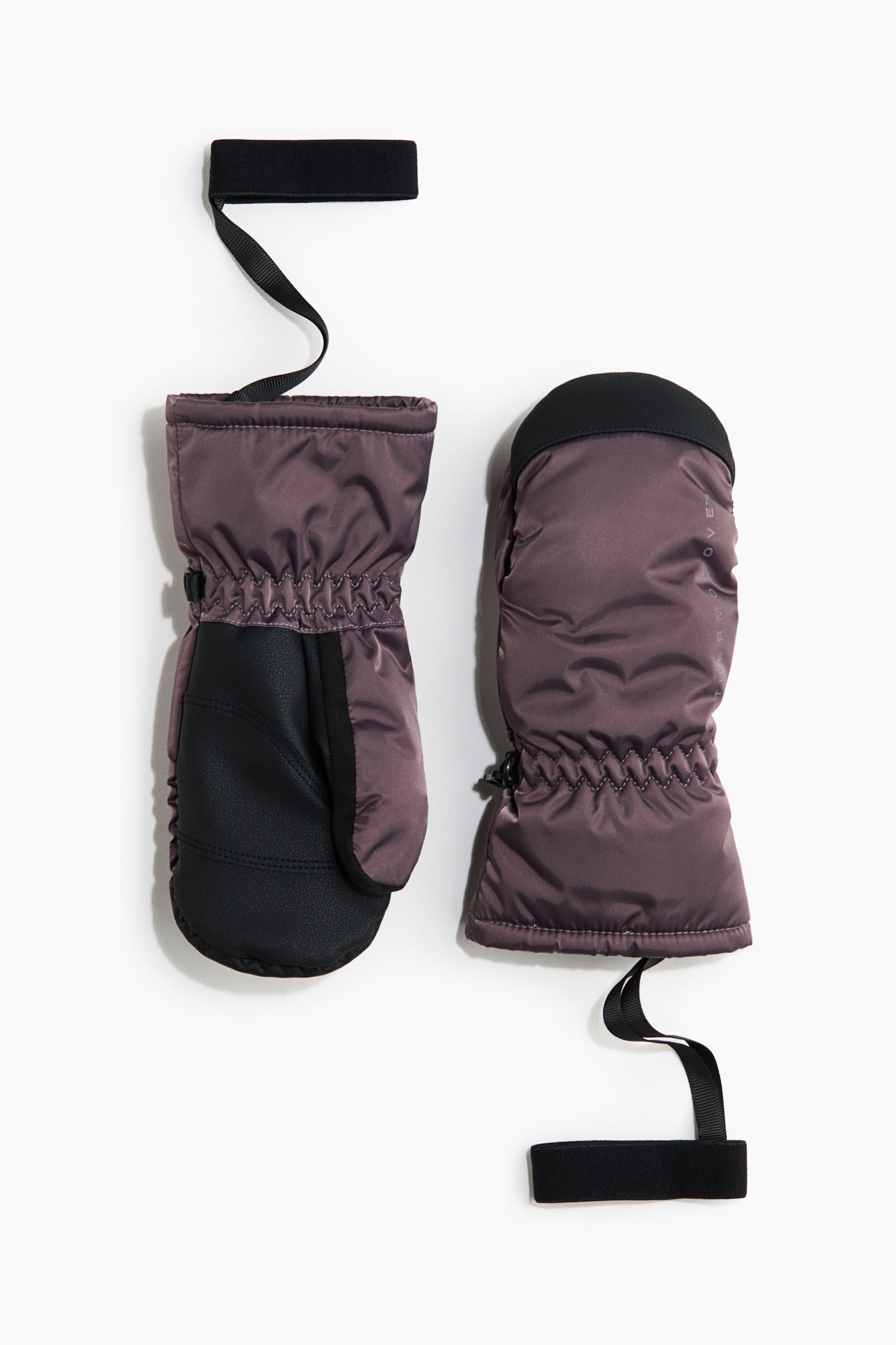 A pair of insulated, mauve-purple mittens is lying flat, with one showing the front palm side and the other showing the back. The mittens feature gathered elastic wrists and attached black elastic wrist straps. A black textured grip covers the palm of one mitten, while a black reinforced patch tops the other. - 1