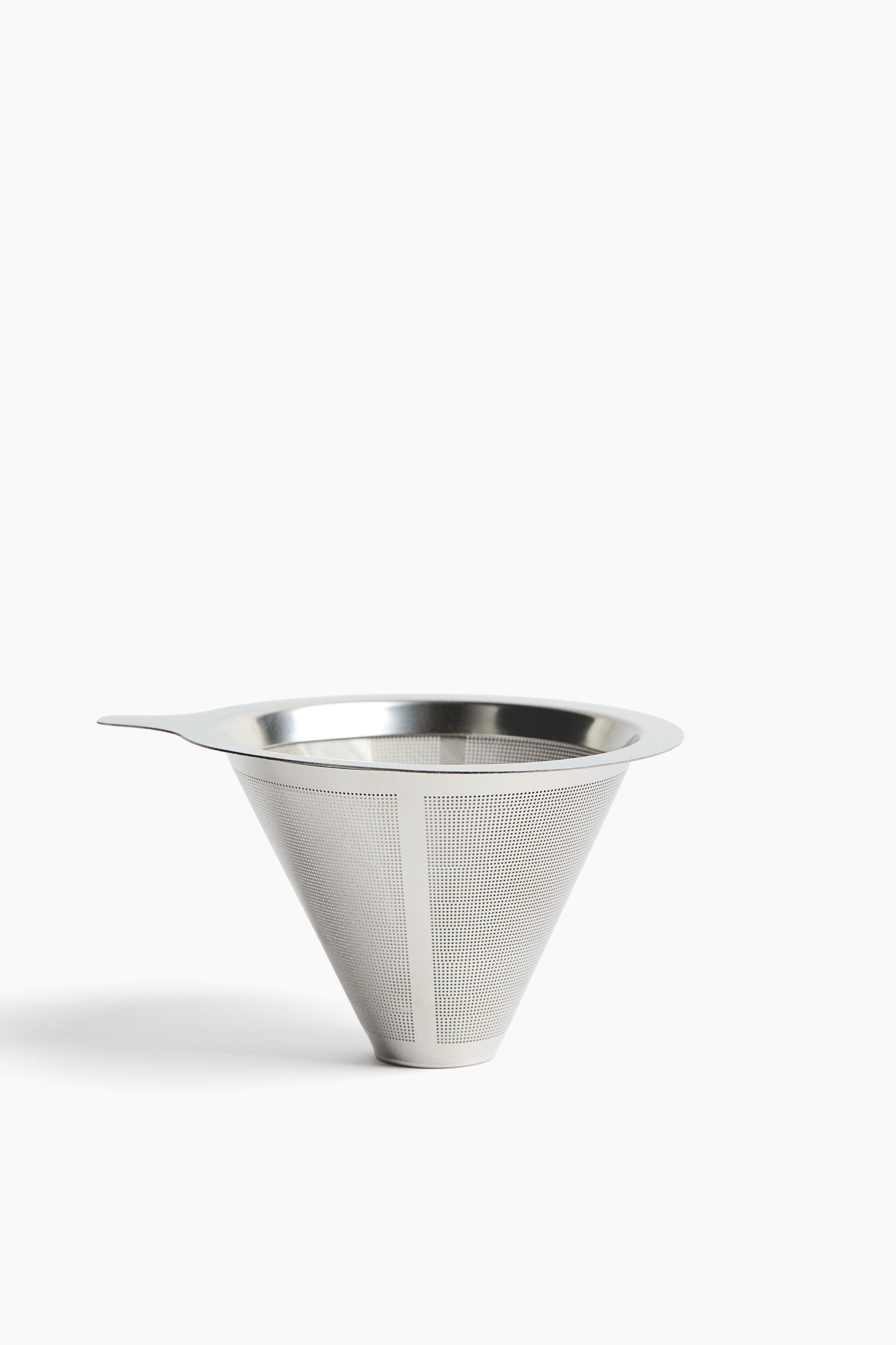 View larger image: A conical stainless steel pour-over coffee filter is positioned at a slight angle, showcasing its finely perforated cone with distinct vertical perforated bands, a wide flat rim, and a small side tab.