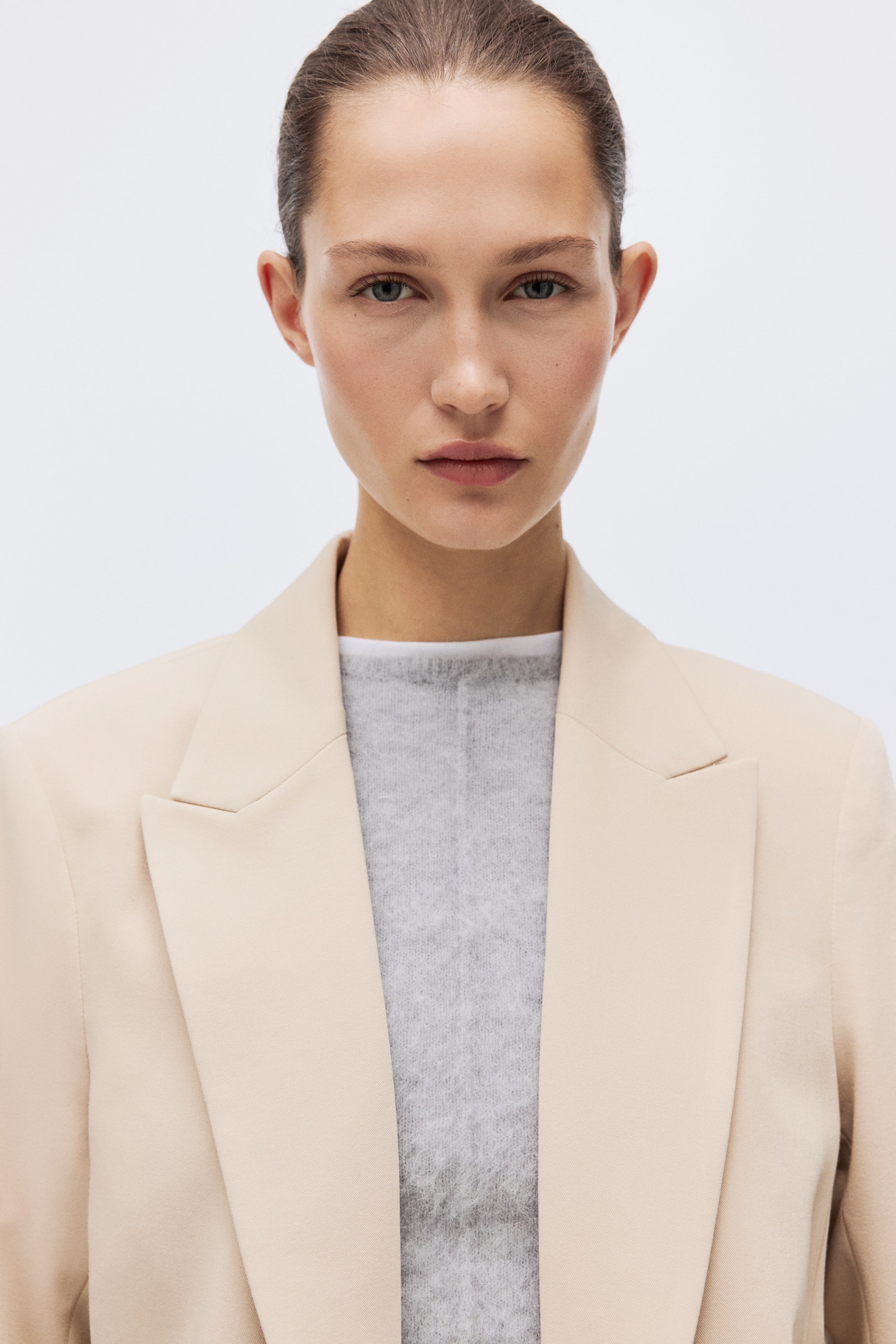 View larger image: The model wears a blazer with peak lapels and an open front, layered over a light gray sweater.