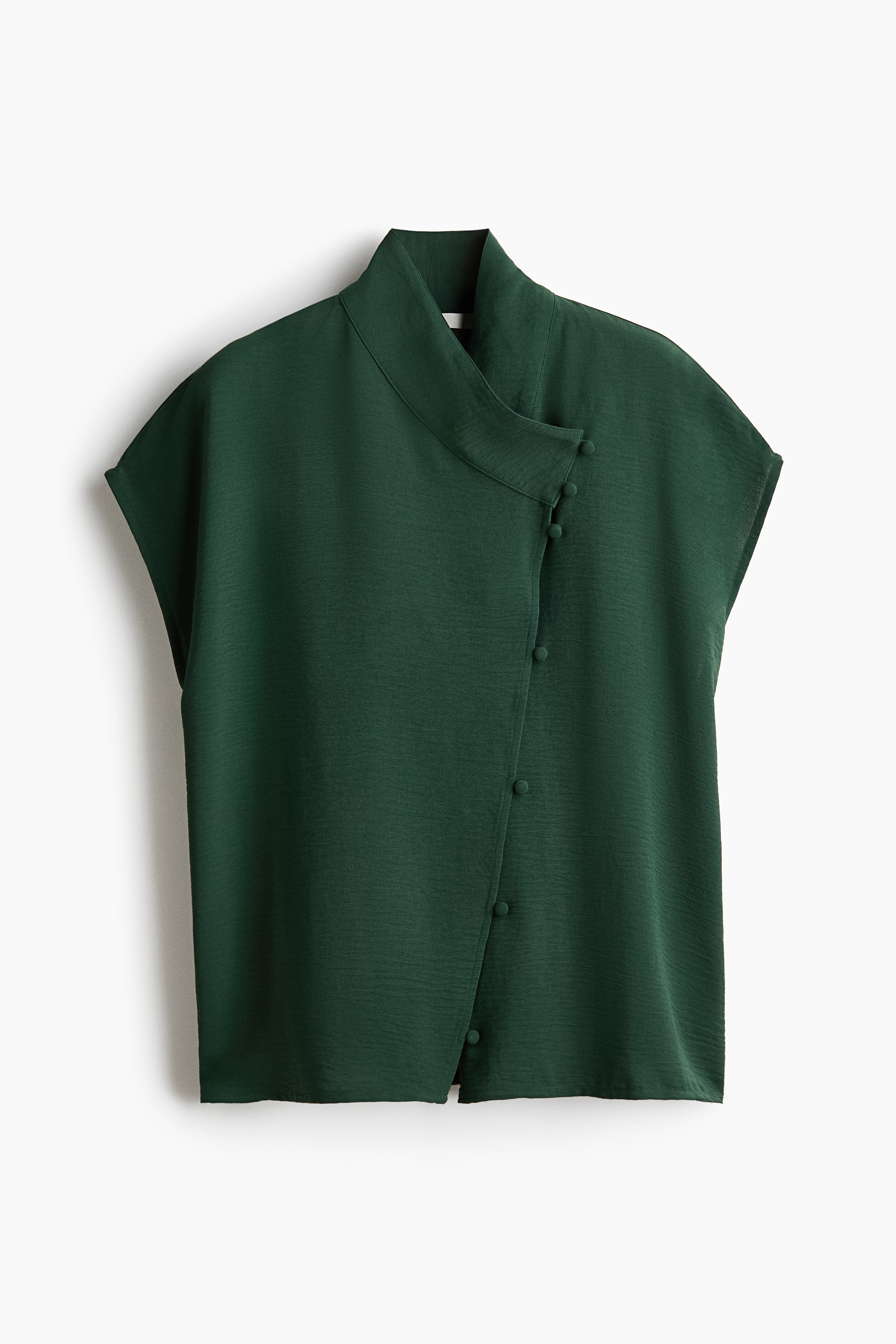 La modelo lleva una blusa tejida en verde oscuro con escote cruzado alto, mangas tipo cap y una abertura frontal descentrada con botones forrados. La blusa se combina con un pantalÃ³n a juego en verde oscuro.