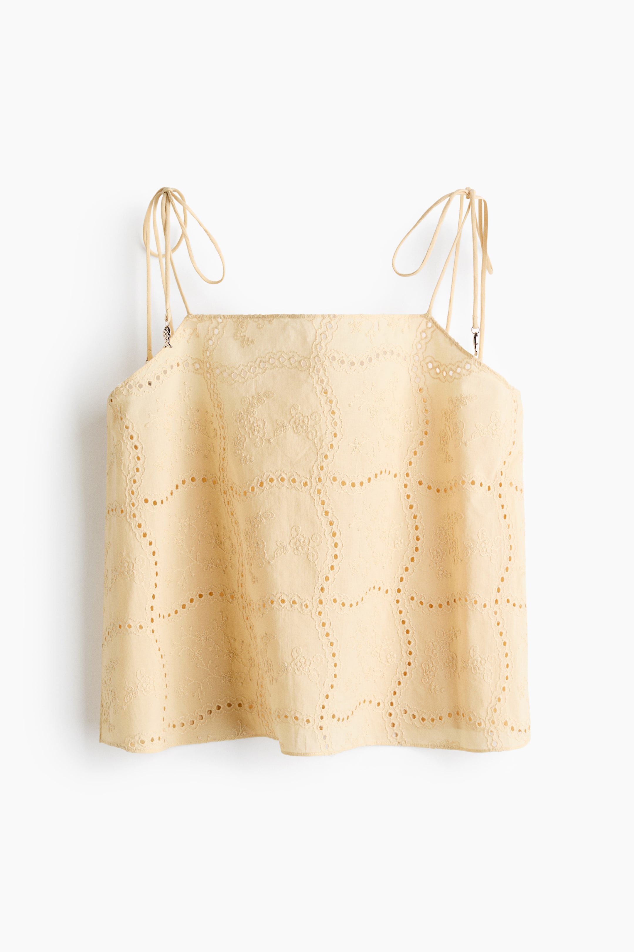 View larger image: A light yellow square-neck top is shown FRONT, featuring tie-up shoulder straps. The top is made from fabric with broderie anglaise detailing, forming a repeating pattern of floral motifs set within squares, alongside wavy lines of eyelet embroidery.