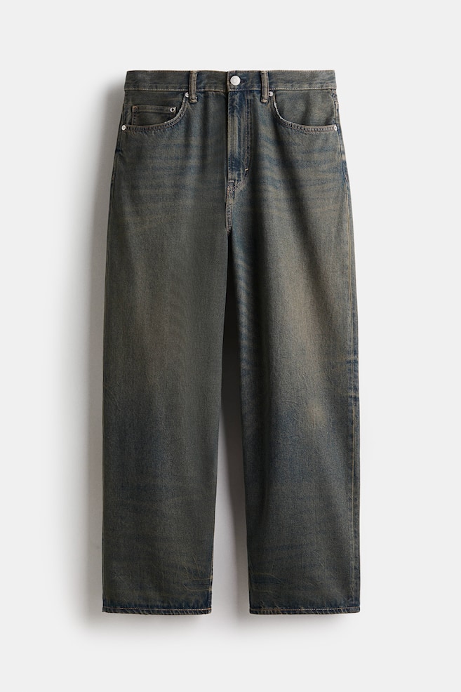 Un par de vaqueros de 5 bolsillos orientados hacia adelante muestran un lavado oscuro y descolorido en denim de algodón rígido. Están diseñados con una cintura regular, una bragueta con cremallera y un ajuste holgado a lo largo de la pierna redondeada, con una entrepierna caída y una apariencia apilada en el tobillo. - 1