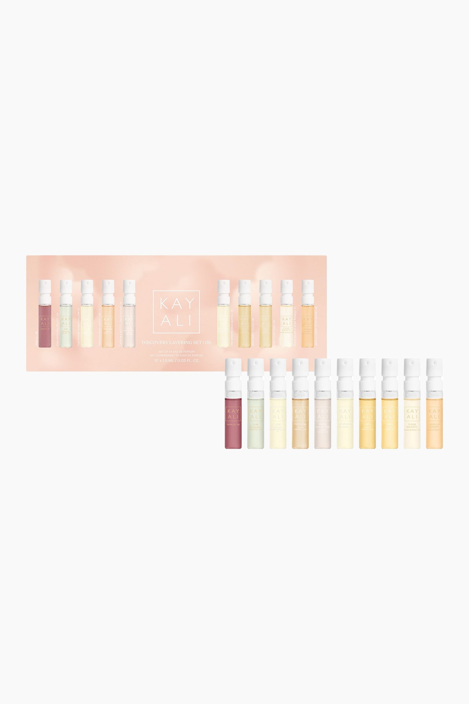 Kayali Discovery Layering Set \| 06 visar tio små glasflaskor med parfymprover, placerade i rad bredvid deras ljusrosa kartongförpackning. Flaskorna har vita spraykorkar och innehåller vätskor i en färgskala från mauve och ljusgrönt till nyanser av gult och bärnsten.