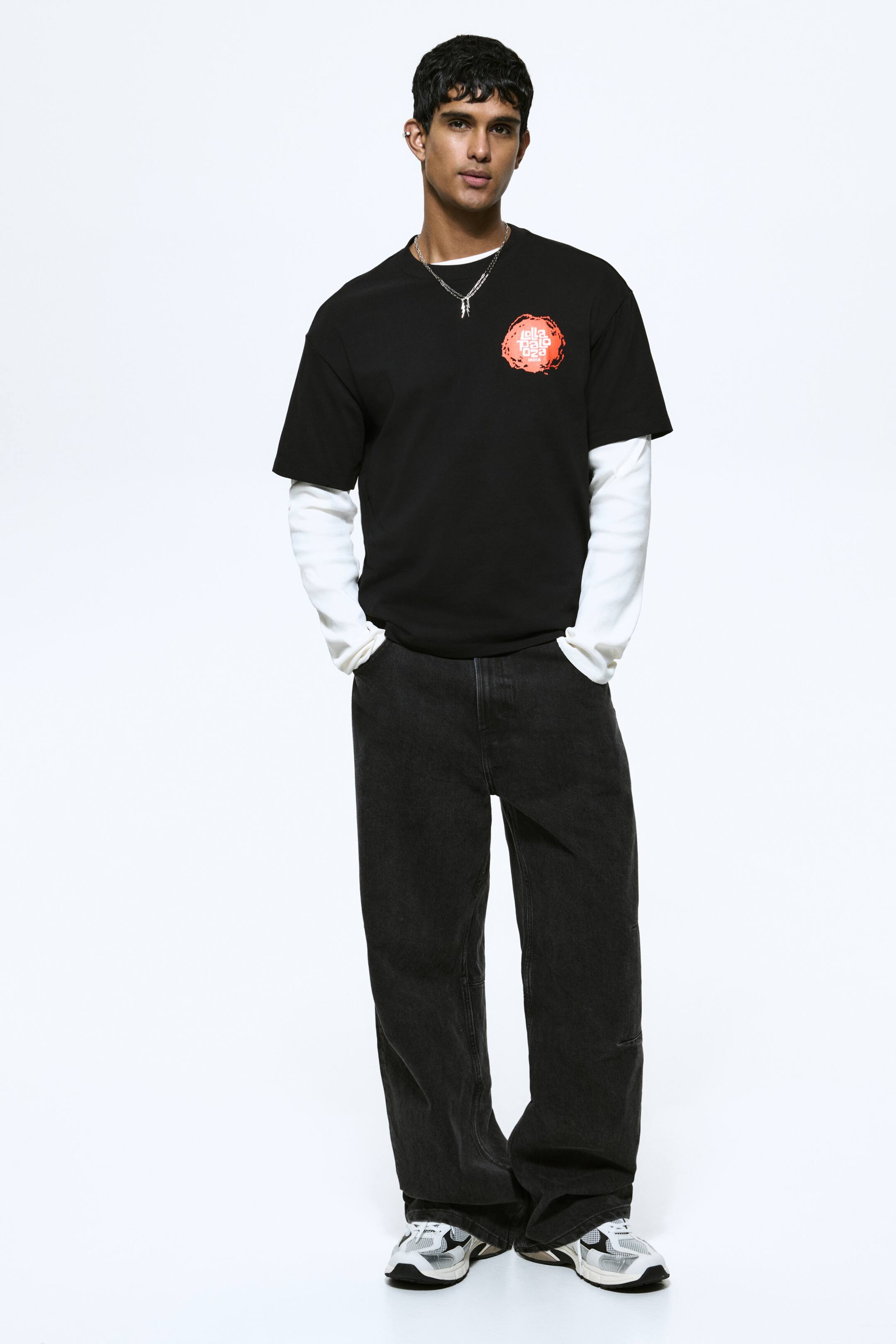 View larger image: A black short-sleeve crew-neck T-shirt featuring a circular orange and white graphic with the text “illa dalla ibiza” on the left chest. Styled layered over a white long-sleeve shirt, with the white sleeves extending beyond the T-shirt’s short sleeves.