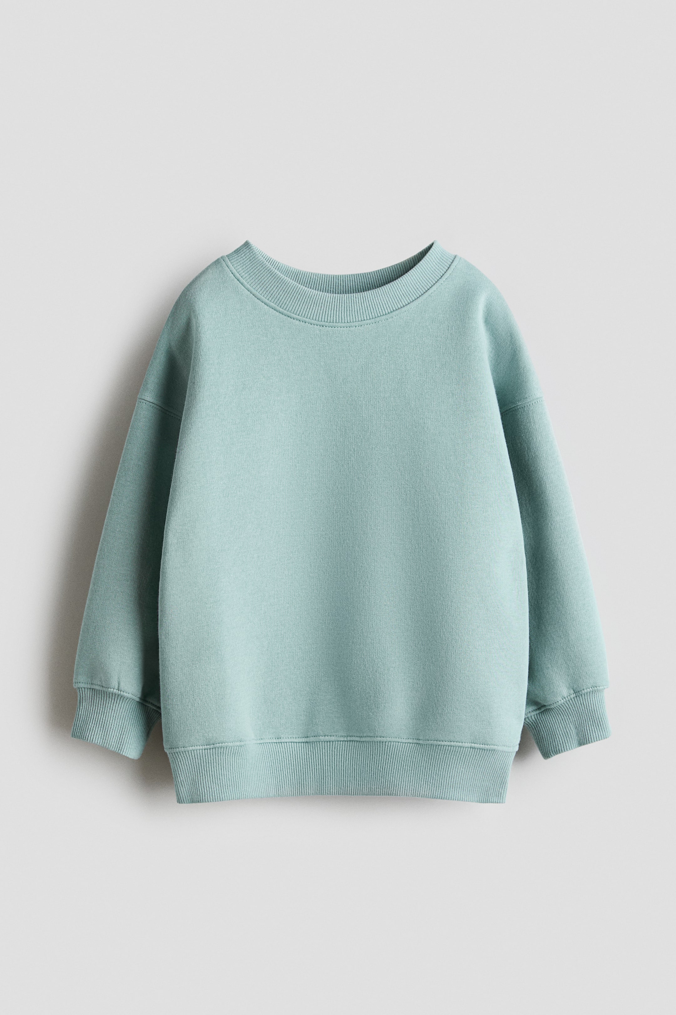 Agrandir l'image: Un sweat oversize bleu-vert clair, présenté de face, arbore un col rond à finition côtelée. Il est conçu avec des épaules tombantes, des manches longues à poignets côtelés et un ourlet côtelé.
