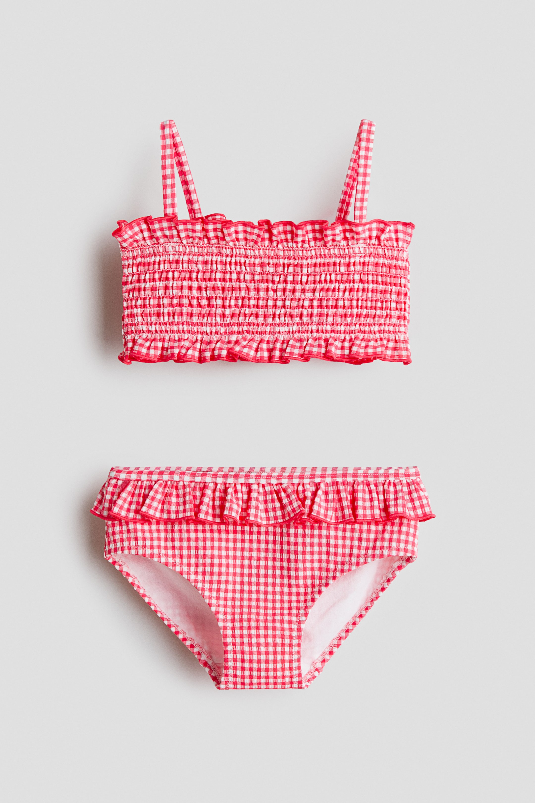 View larger image: The H&M Adorables bikini set showcases a red and white gingham pattern on textured fabric. The FRONT top features smocking, frill trim, and narrow, elasticated shoulder straps, while the matching bottoms display a frill trim around the waist.