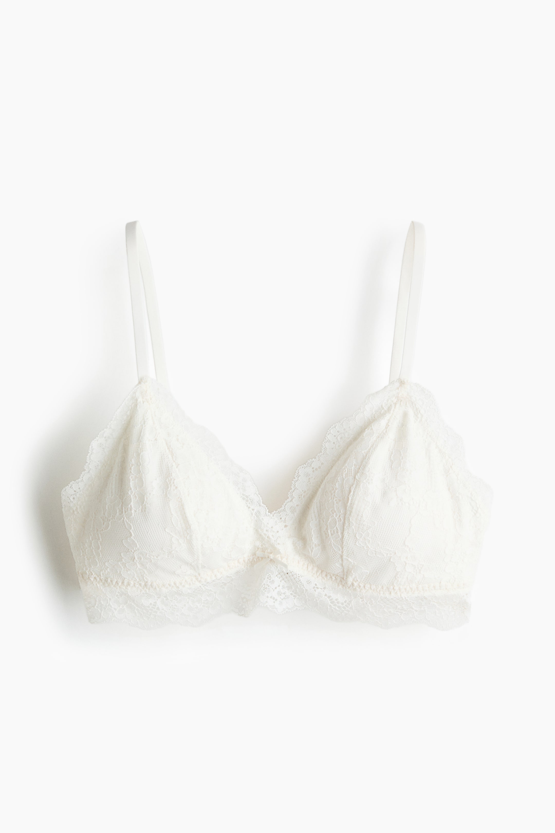 Ampliar la imagen: Un bralette de encaje color crema se muestra de frente, con copas triangulares y ribete de encaje festoneado en los bordes superior e inferior, tirantes delgados y una banda elástica estrecha en la parte inferior.