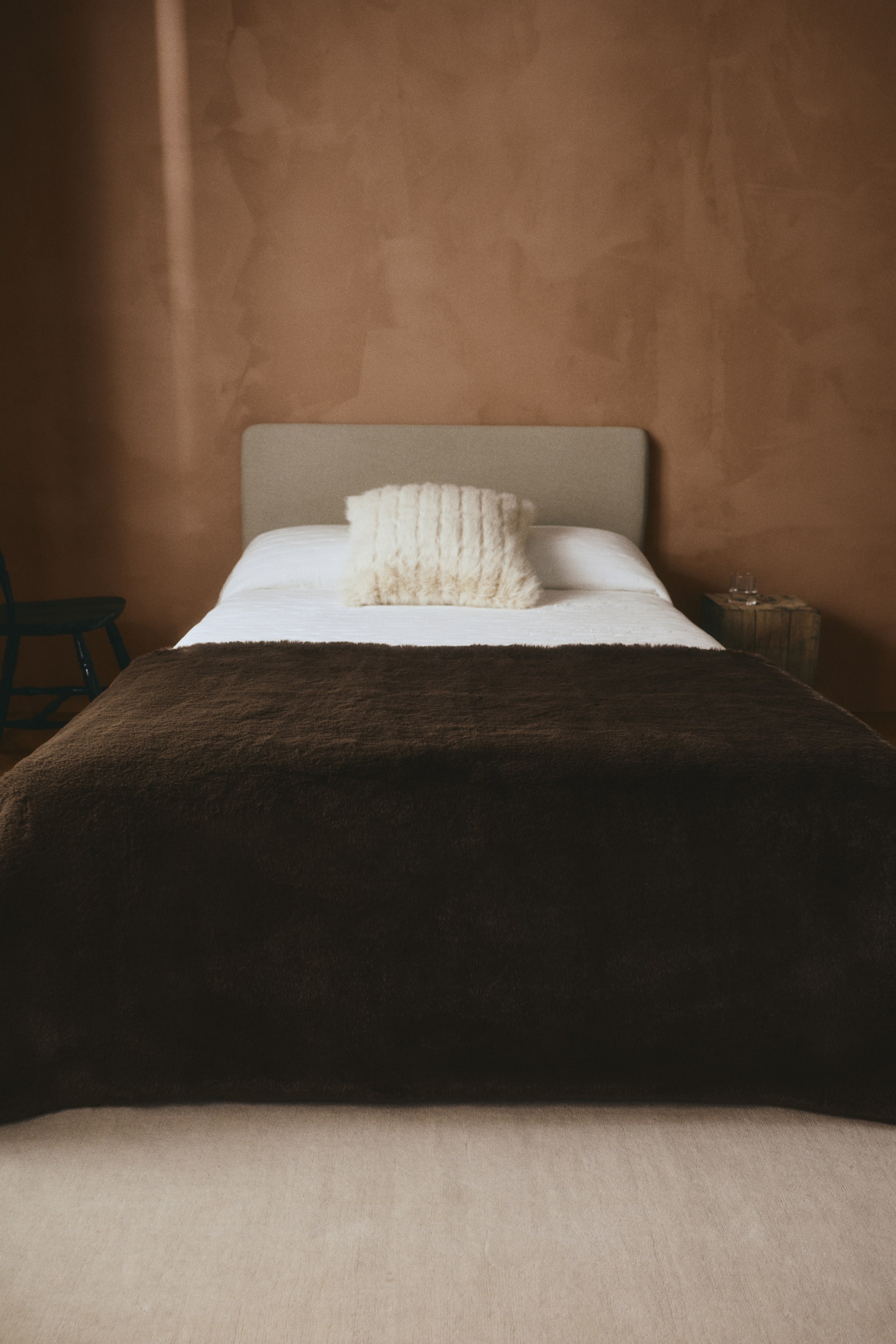 Agrandir l'image: Une couverture duveteuse brun foncé est étendue à plat sur la partie inférieure d’un lit, par-dessus des draps blancs, mettant en valeur sa texture moelleuse à poils longs. La couverture retombe sur le pied et les côtés du lit, soulignant son tissu doux et épais.