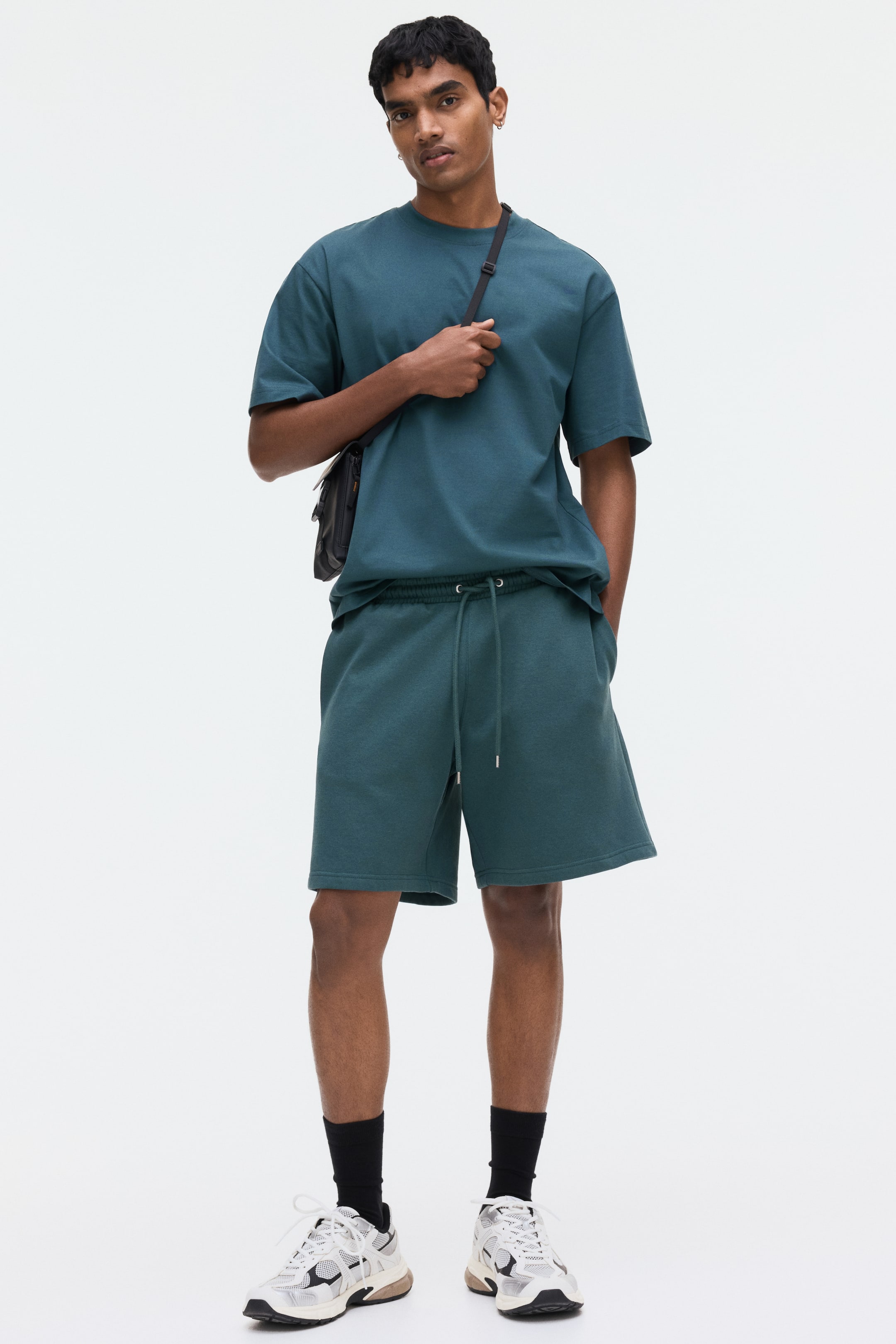 View larger image: A matching teal t-shirt and shorts set is displayed facing forward. The oversized t-shirt features short sleeves and a crew neck, while the relaxed-fit shorts showcase an elasticated drawstring waistband with metal tips, reaching to the knees.