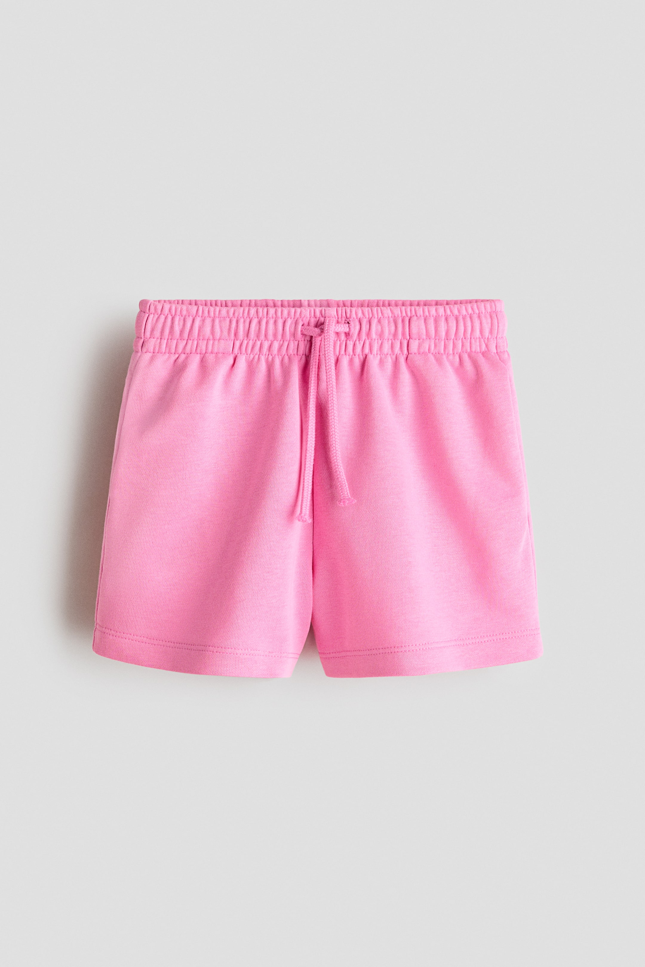 Grotere afbeelding bekijken: Roze shorts met een elastische tailleband en een trekkoord dat aan de voorkant in een knoop is vastgebonden. Ze zijn gemaakt van een lichte sweatshirtstof.