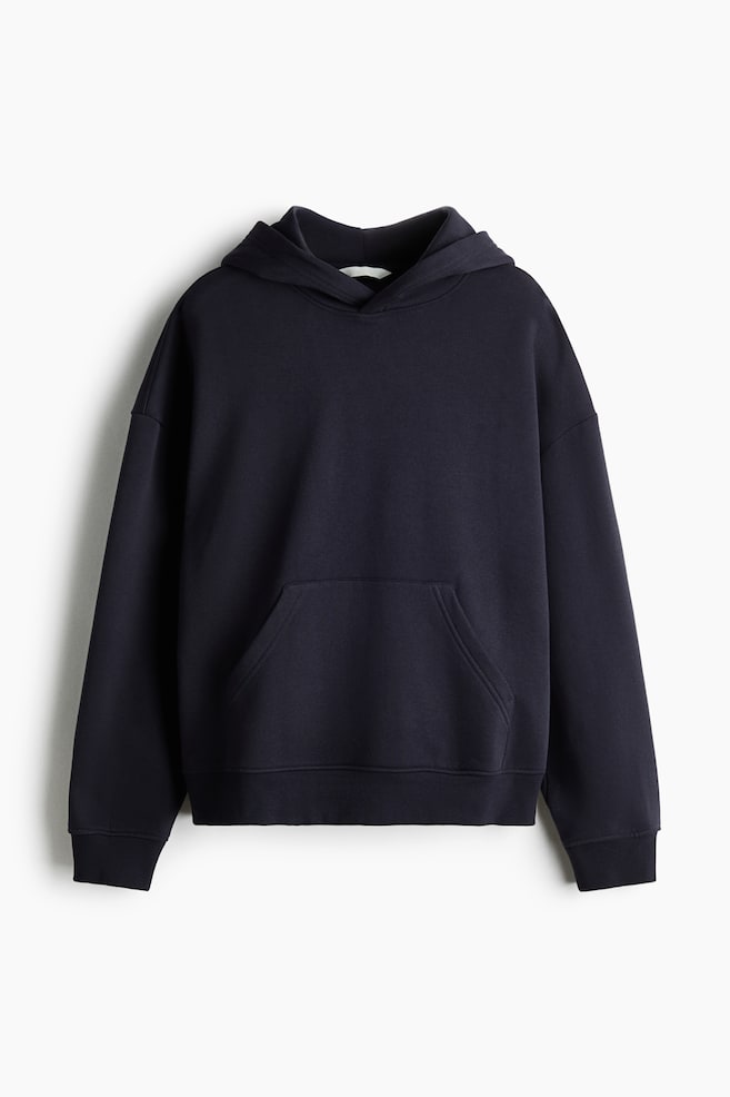 Se muestra una sudadera con capucha de color azul marino oscuro vista de frente, con capucha de doble capa, hombros caÃdos y un bolsillo canguro central. El diseño se completa con puños acanalados y bajo acanalado. - 1