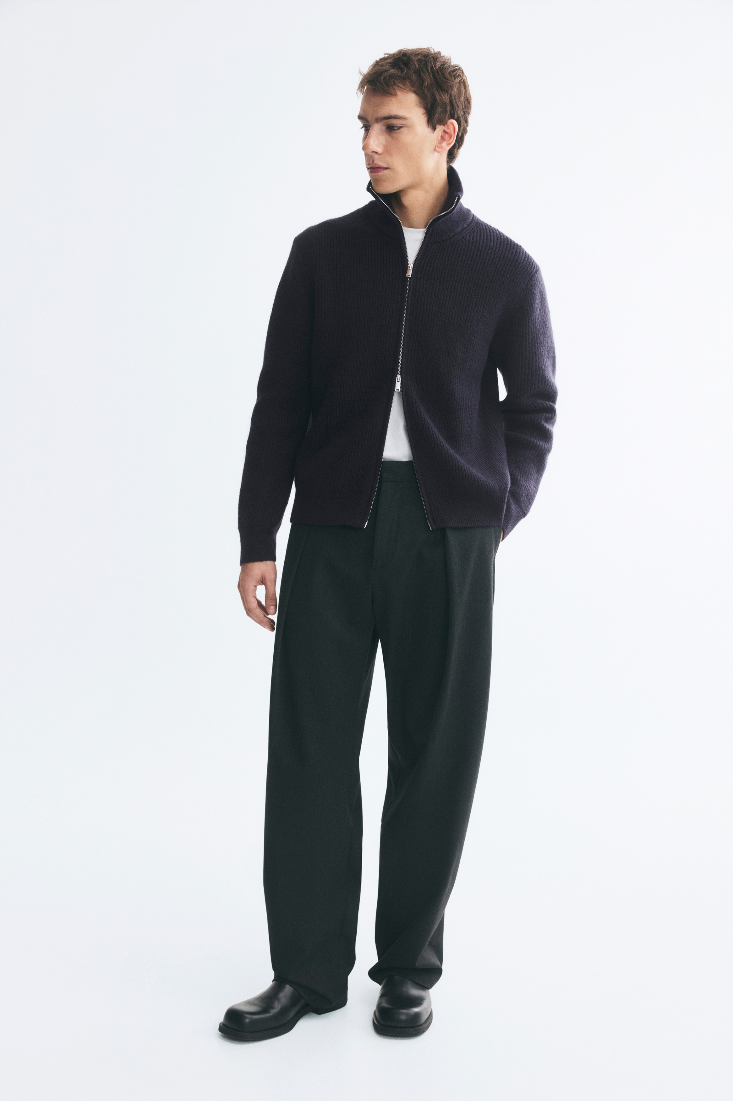 A navy blue rib-knit cardigan is displayed from the front, featuring a high stand collar, a two-way front zip fastening, and long sleeves. The garment showcases a regular-fit silhouette with a consistent vertical ribbed texture.
